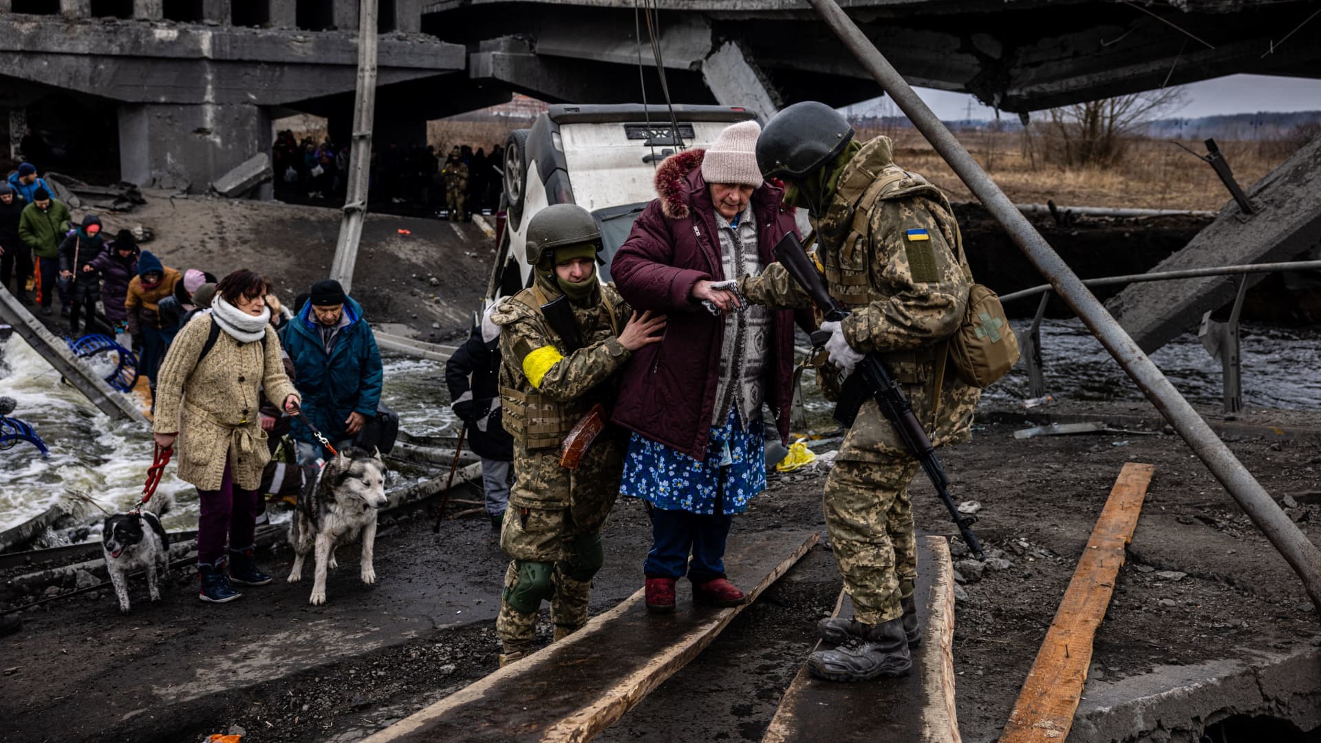 Ukrainian soldiers help an elderly woman to cross a destroyed bridge as she evacuates the city of Irpin, northwest of Kyiv, on March 7, 2022.