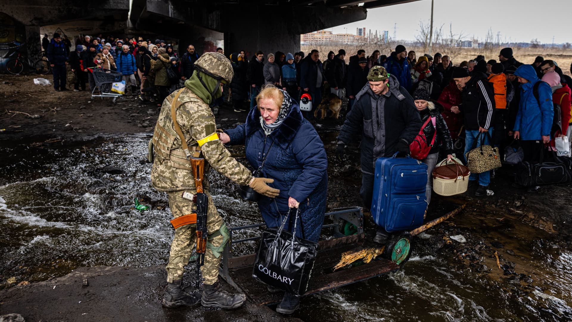 A Ukrainian serviceman helps evacuees gathered under a destroyed bridge as they flee the city of Irpin, northwest of Kyiv, on March 7, 2022.
