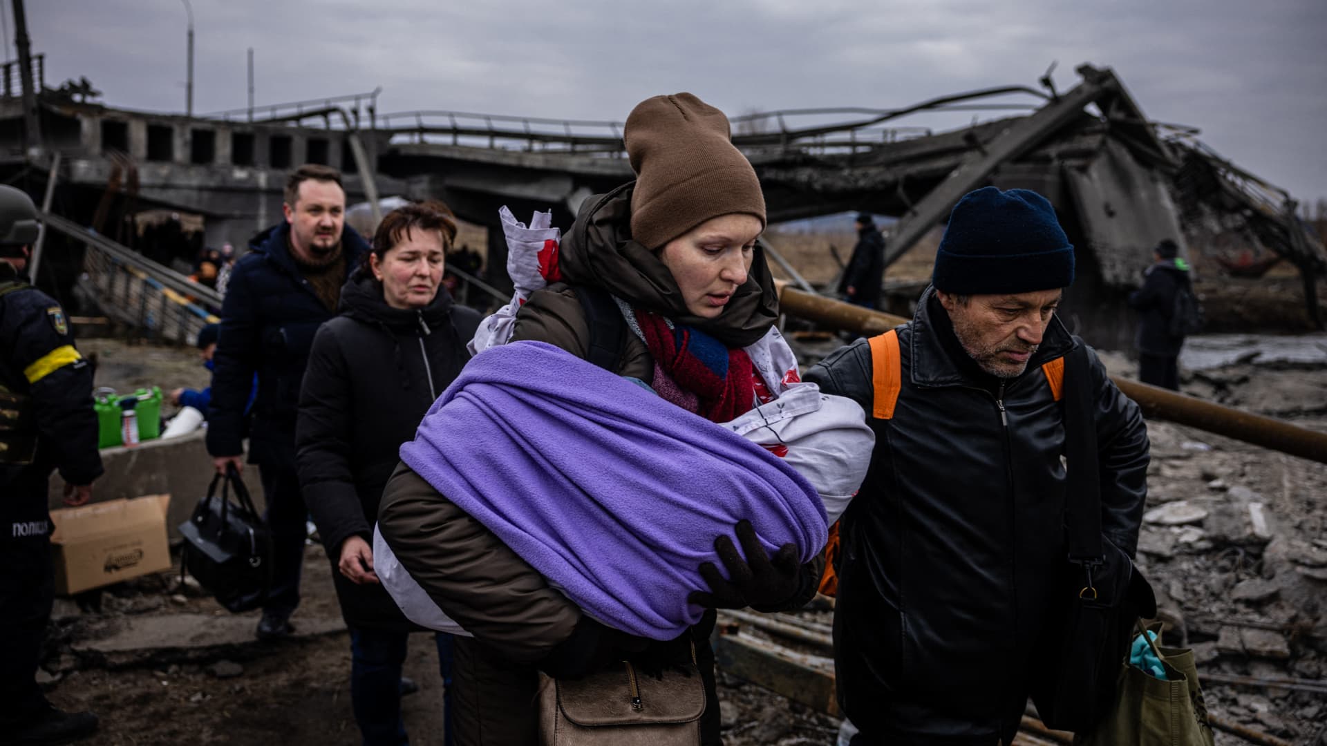 A woman carrying her baby crosses a destroyed bridge as they flee the city of Irpin, northwest of Kyiv, on March 7, 2022.