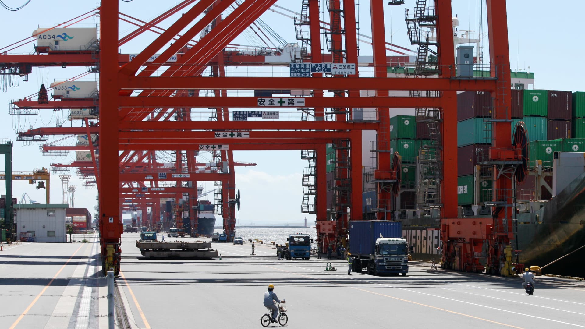 A worker cycles past a ship at a shipping terminal in Tokyo, Japan.