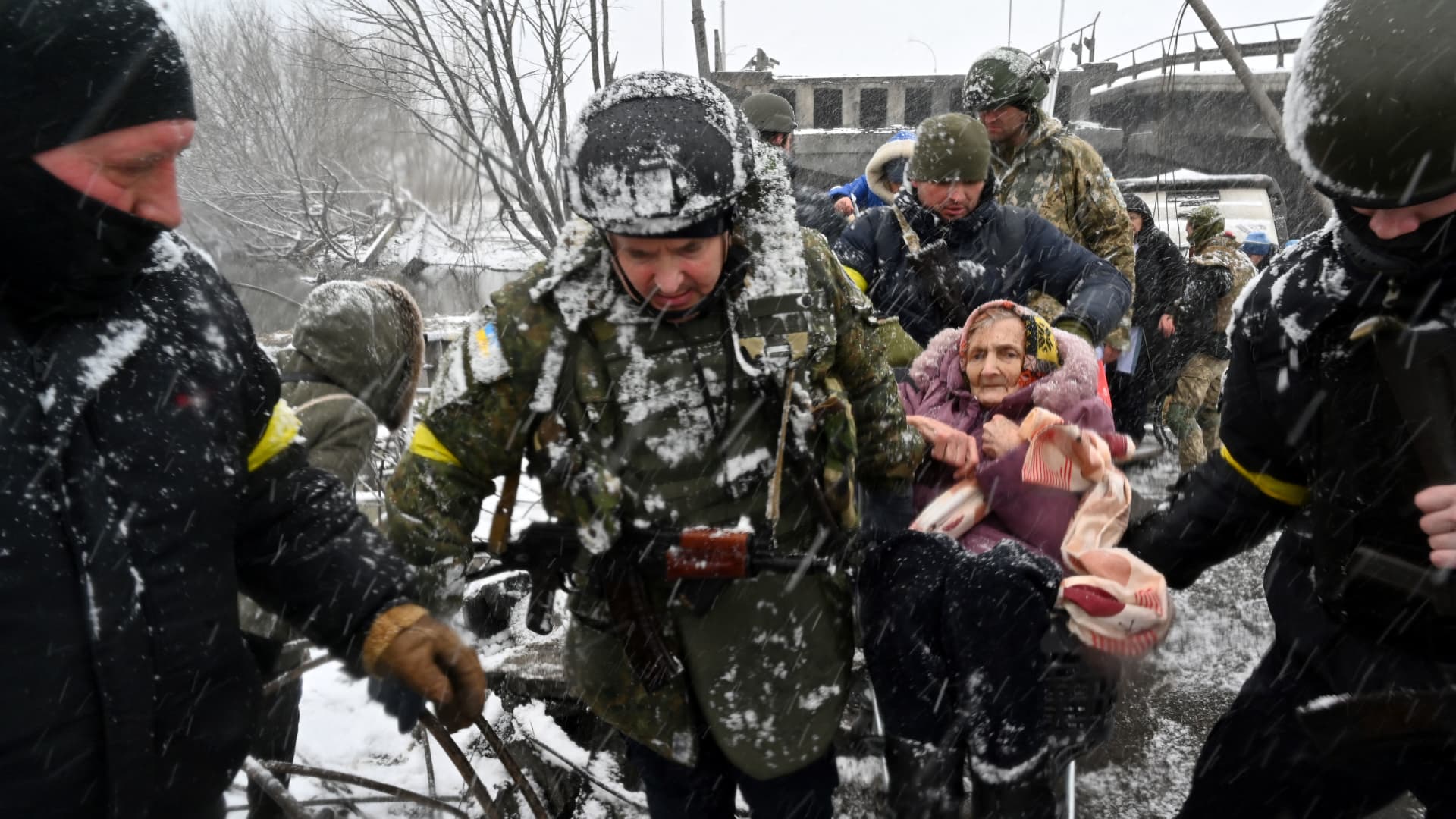 Ukrainian soldiers help an elderly woman to cross a destroyed bridge as she evacuates the city of Irpin, northwest of Kyiv, on March 8, 2022.