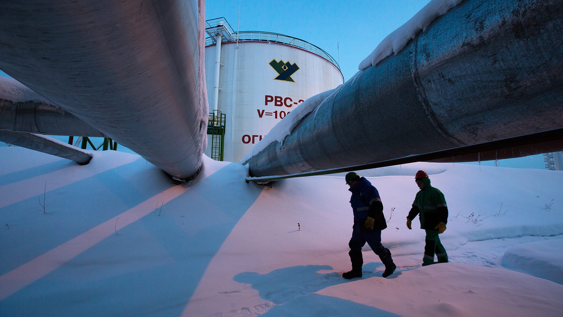Employees pass beneath pipes leading to oil storage tanks at the central processing plant for oil and gas at the Salym Petroleum Development oil fields near the Bazhenov shale formation in Salym, Russia.