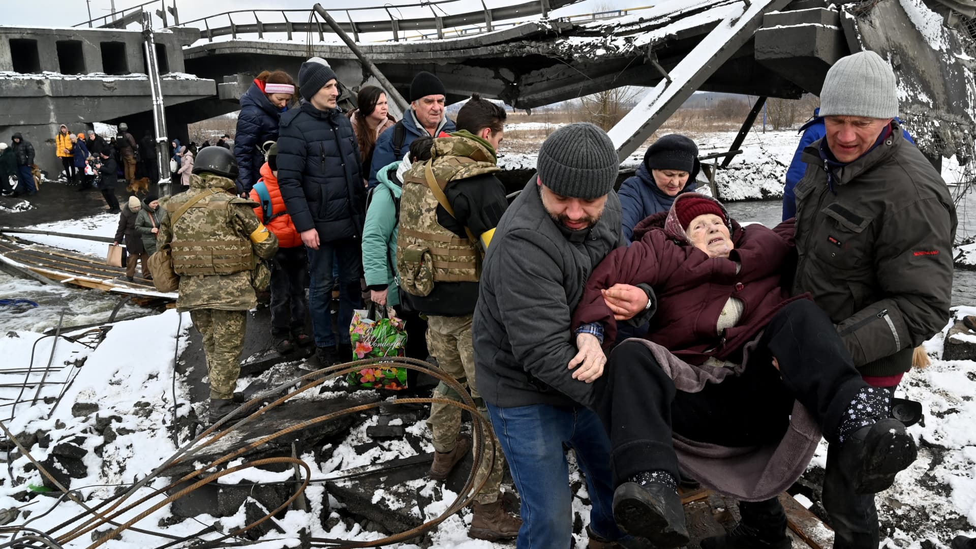 Ukrainian soldiers help an elderly woman to cross a destroyed bridge as she evacuates the city of Irpin, northwest of Kyiv, on March 8, 2022.