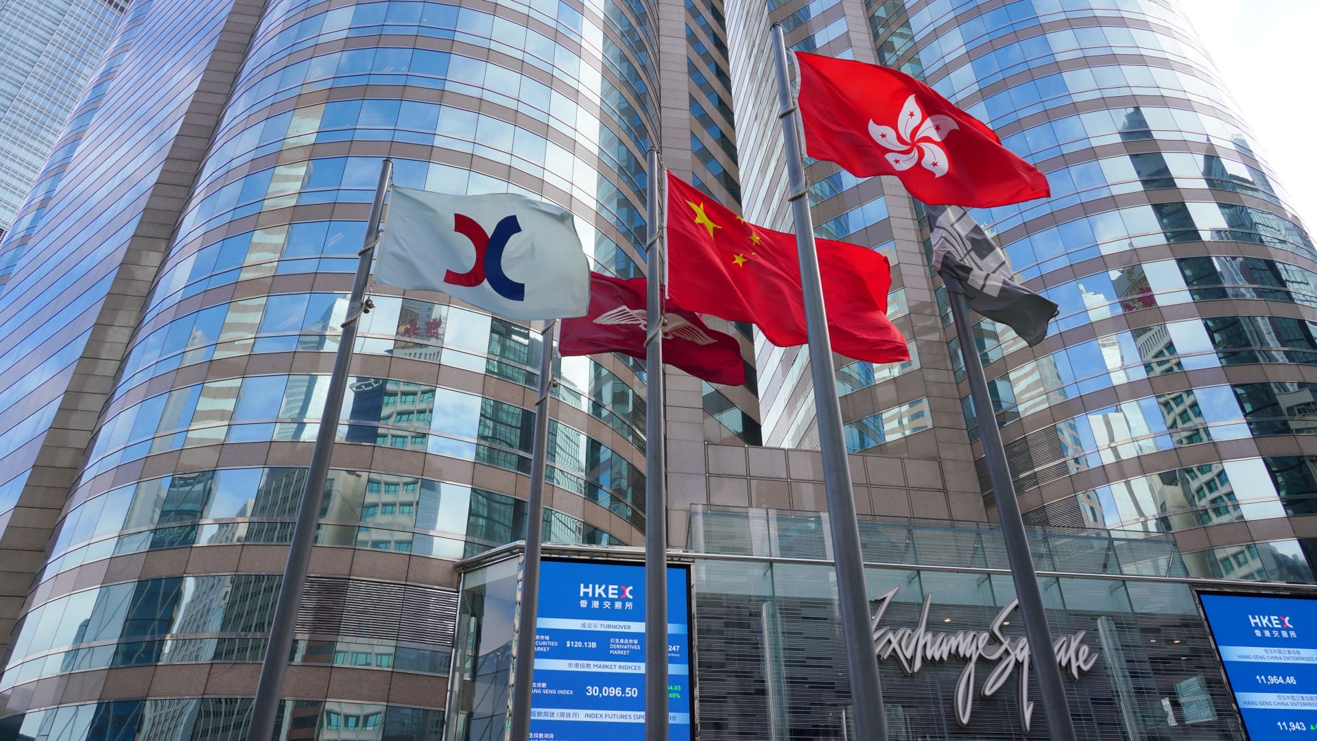 The Chinese and Hong Kong flags flutter as screens display the Hang Seng Index outside the Exchange Square complex, which houses the Hong Kong Stock Exchange, on January 21, 2021 in Hong Kong, China.