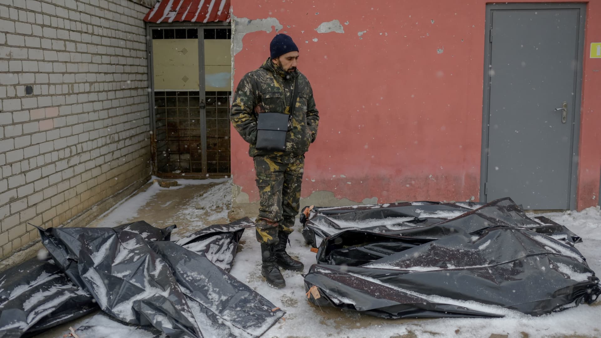 A Ukrainian man in camouflage stands next to snow covered body bags in the yard of a morgue in Mykolaiv, a city on the shores of the Black Sea that has been under Russian attack for days on March 11, 2022.