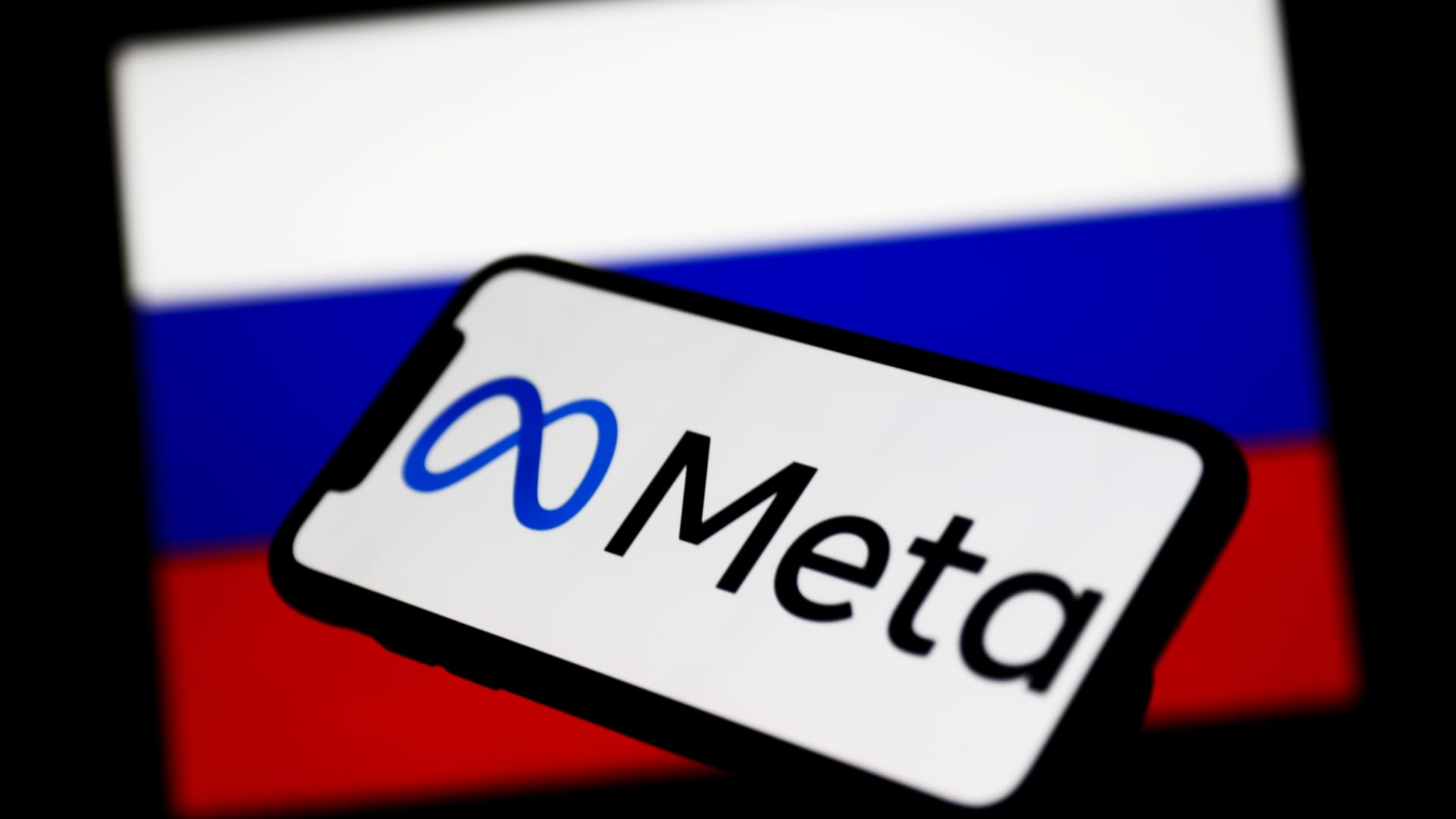 Meta logo displayed on a phone screen and Russian flag displayed on a screen in the background are seen in this illustration photo taken in Krakow, Poland on March 1, 2022.