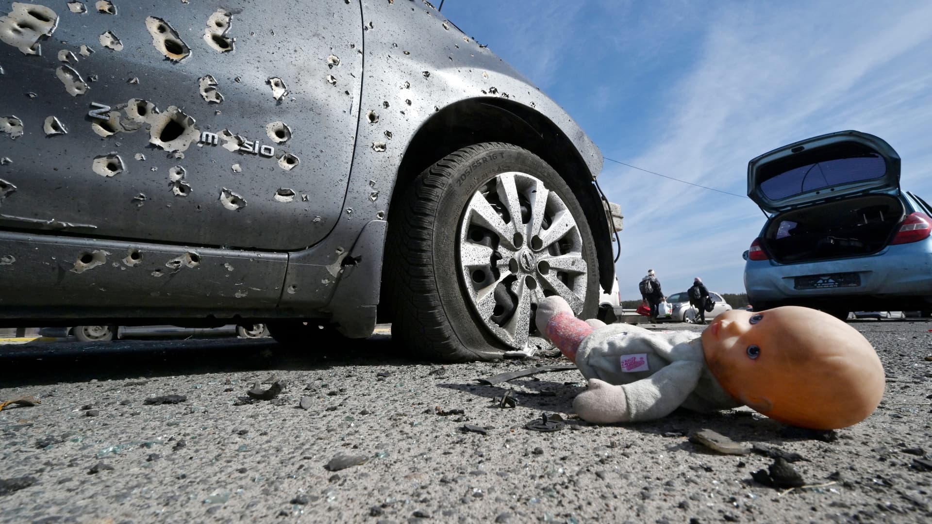 This photograph taken on March 12, 2022 shows an abandoned doll next to a car riddled with bullets in Irpin, north of Kyiv. - Russian forces stepped up the pressure on Kyiv on March 12, 2022.