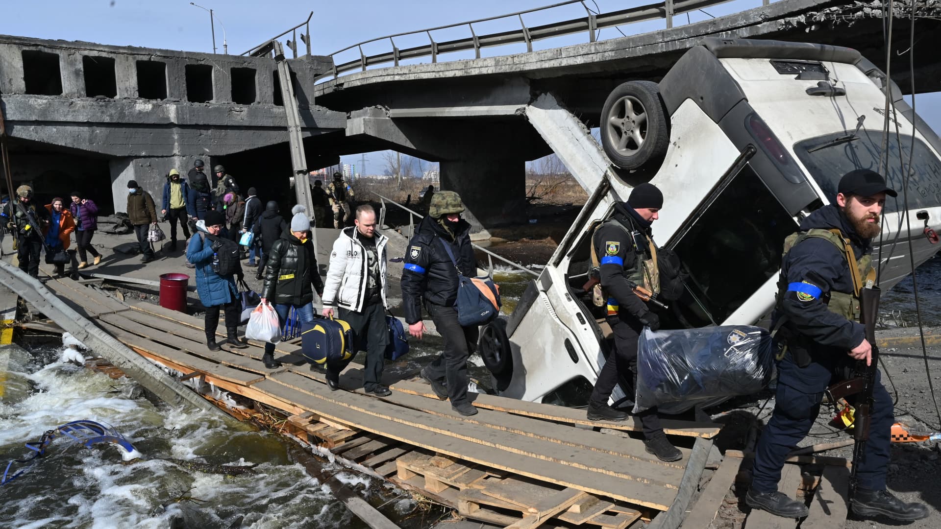 Ukrainian police officers help residents to cross a destroyed bridge as they evacuate Irpin, northwest of Kyiv, on March 12, 2022.