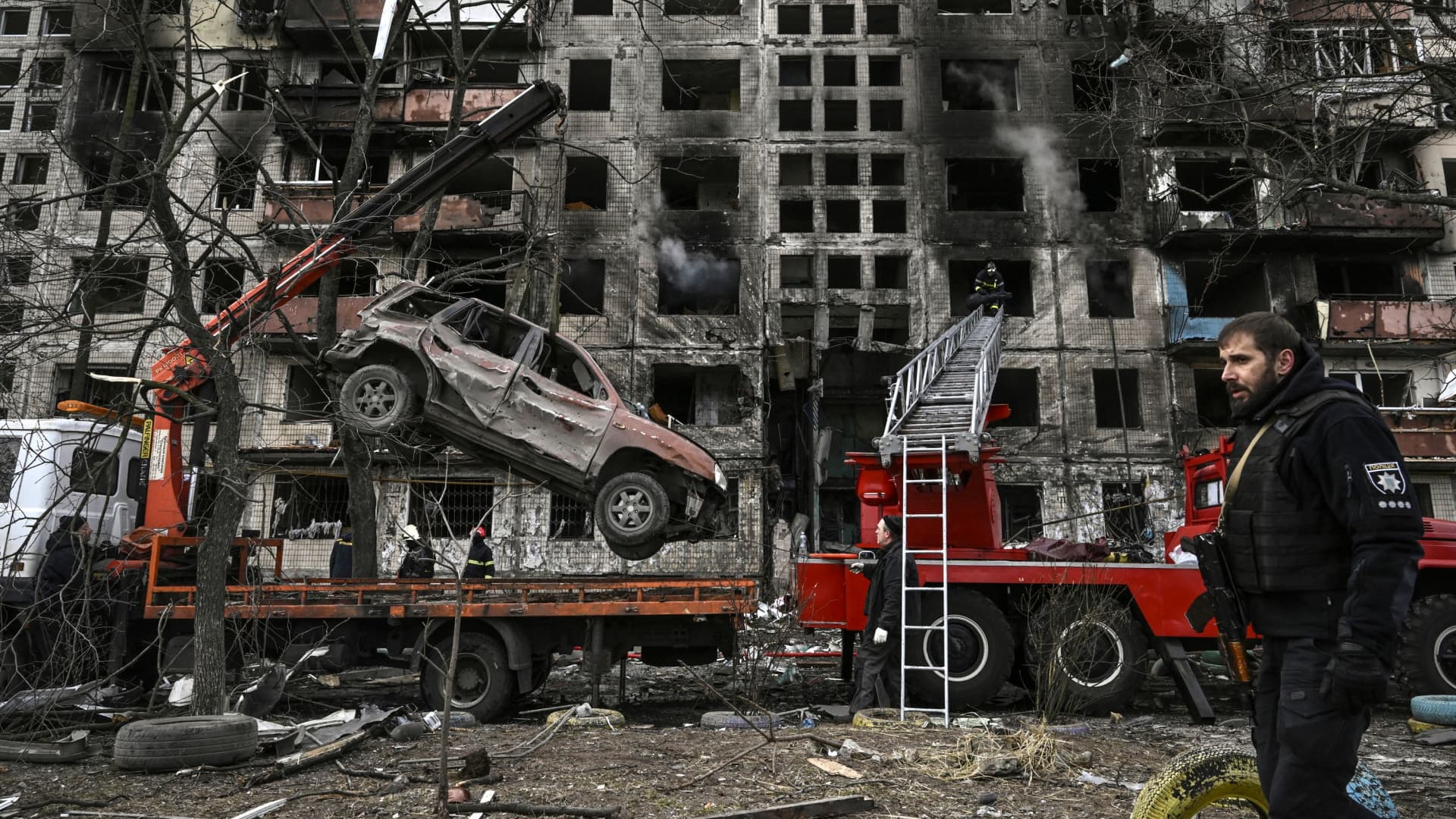 A crane removes a ruined car from in front of a destroyed apartment building after it was shelled in the northwestern Obolon district of Kyiv on March 14, 2022.