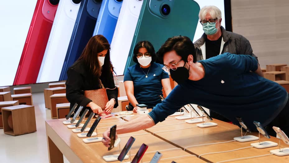 An employee arranges Apple iPhones as customer shop at an Apple store.