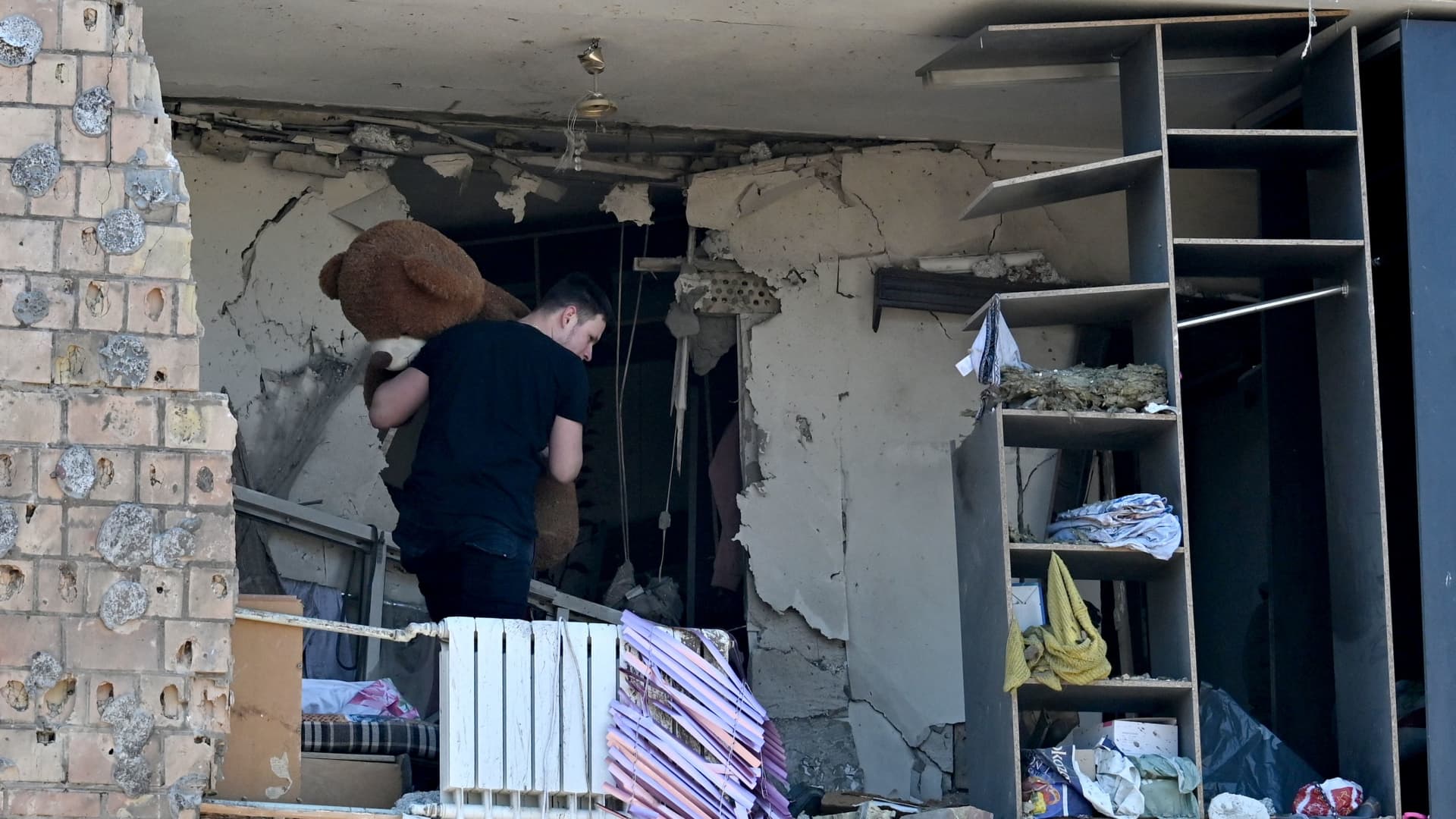 A local resident carries a teddy bear out of his apartment in Kyiv on March 20, 2022 located in a five-storey residential building that partially collapsed after shelling the day before by Russian troops trying to encircle the Ukrainian capital as part of their slow-moving offensives.