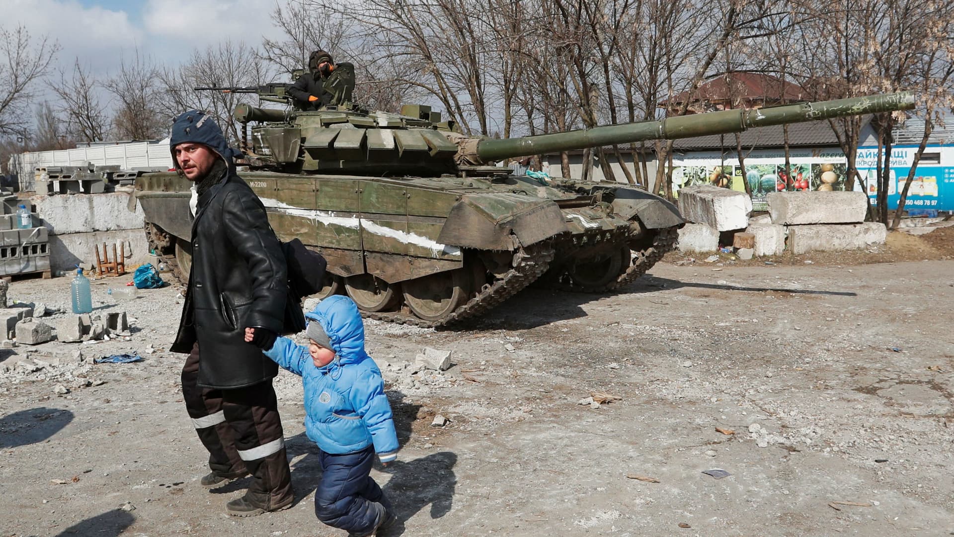 A local resident walks with a child past a tank of pro-Russian troops during Ukraine-Russia conflict in the besieged southern port city of Mariupol, Ukraine March 18, 2022.