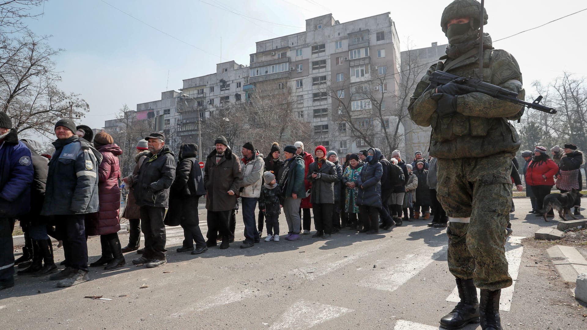A Russian army soldier stands next to local residents who queue for humanitarian aid delivered during Ukraine-Russia conflict, in the besieged southern port of Mariupol, Ukraine March 23, 2022.