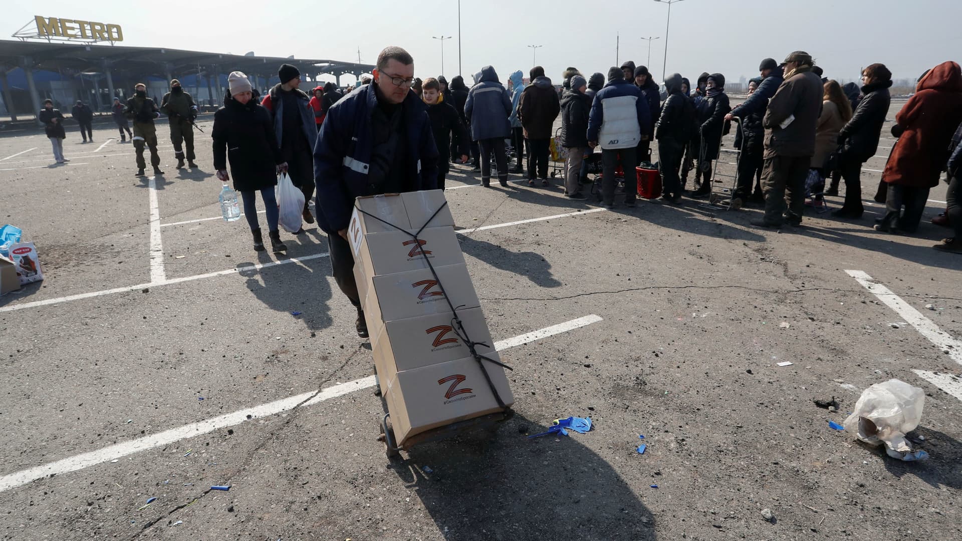 People stand in a long queue during the distribution of humanitarian aid near a damaged store of wholesaler Metro in the besieged southern port city of Mariupol, Ukraine March 24, 2022.