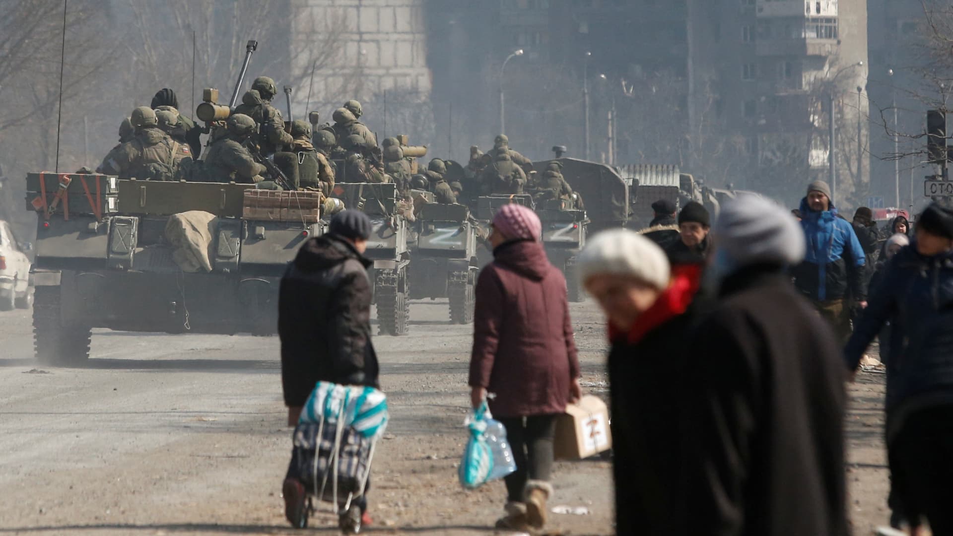 Service members of pro-Russian troops drive armoured vehicles past local residents in the besieged southern port city of Mariupol, Ukraine March 24, 2022.