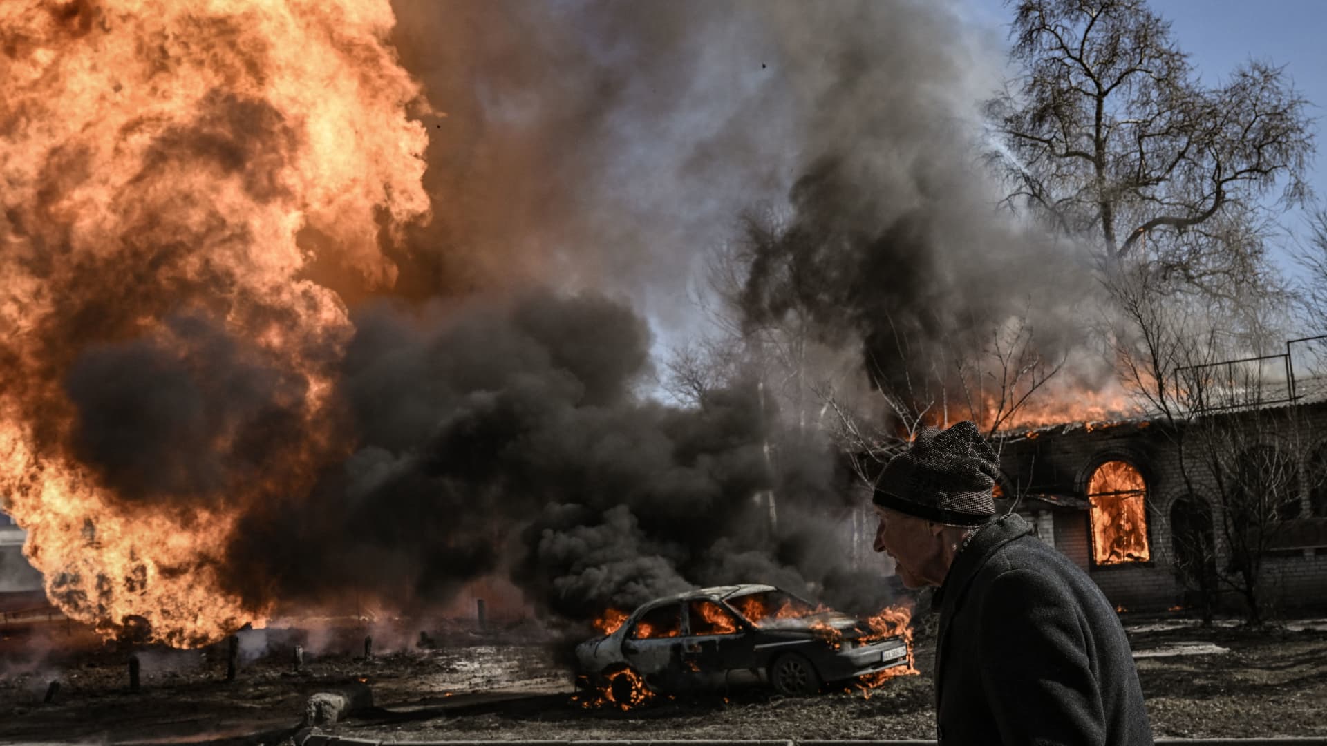 A Ukrainian woman walks past flames and smoke rising from a fire following an artillery fire on the 30th day of the invasion of Ukraine by Russian forces in the northeastern city of Kharkiv on March 25, 2022.