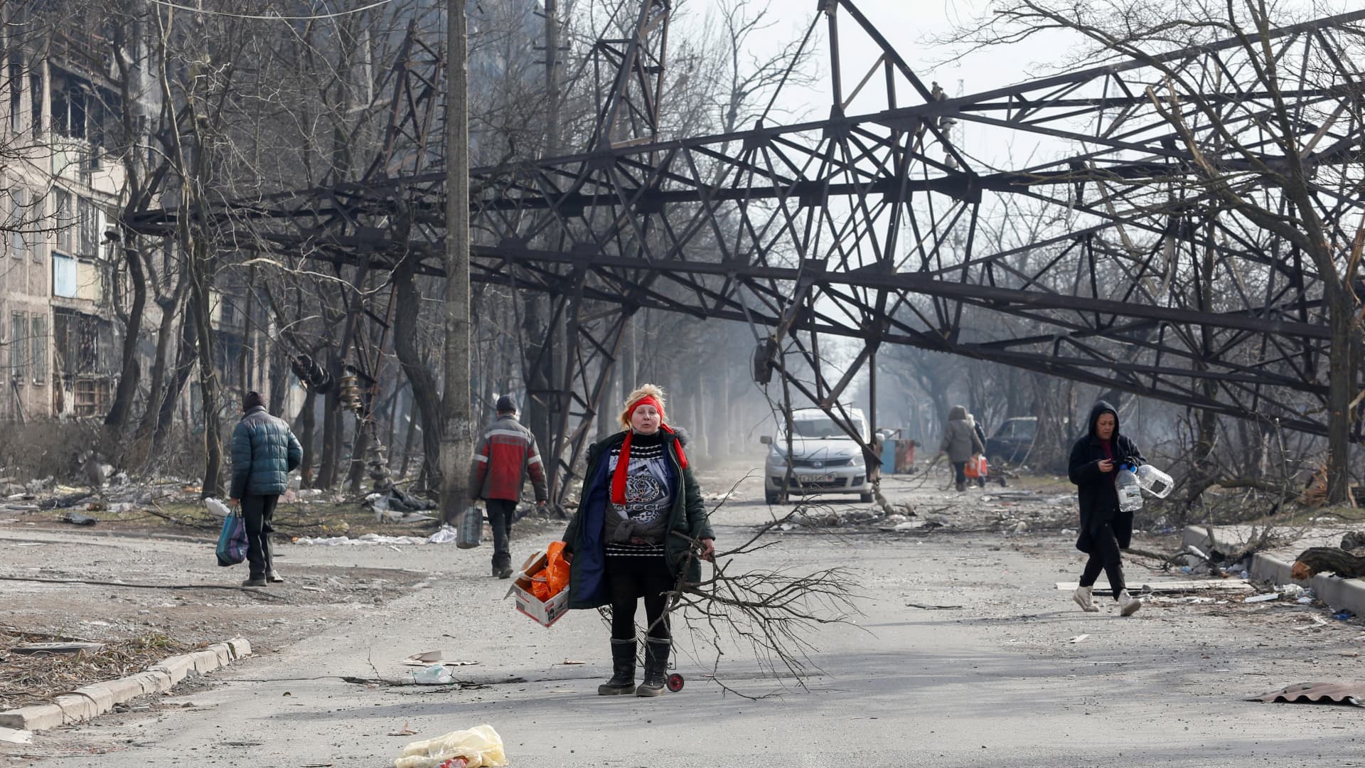 Local residents walk near a fallen electricity pylon and an apartment building destroyed in the course of Ukraine-Russia conflict in the besieged southern port city of Mariupol, Ukraine March 25, 2022.