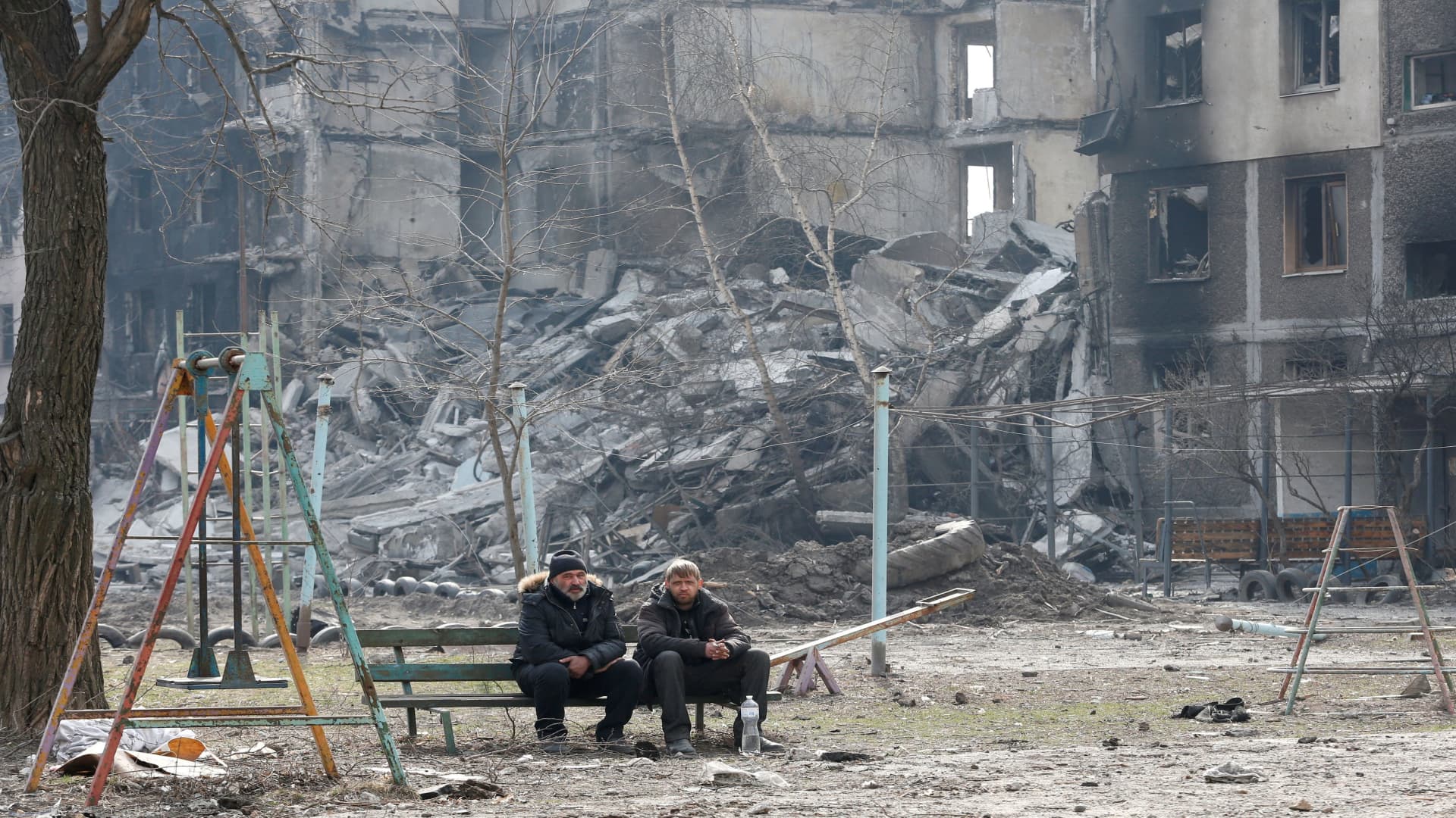 Local residents sit on a bench near an apartment building destroyed in the course of Ukraine-Russia conflict in the besieged southern port city of Mariupol, Ukraine March 25, 2022. 