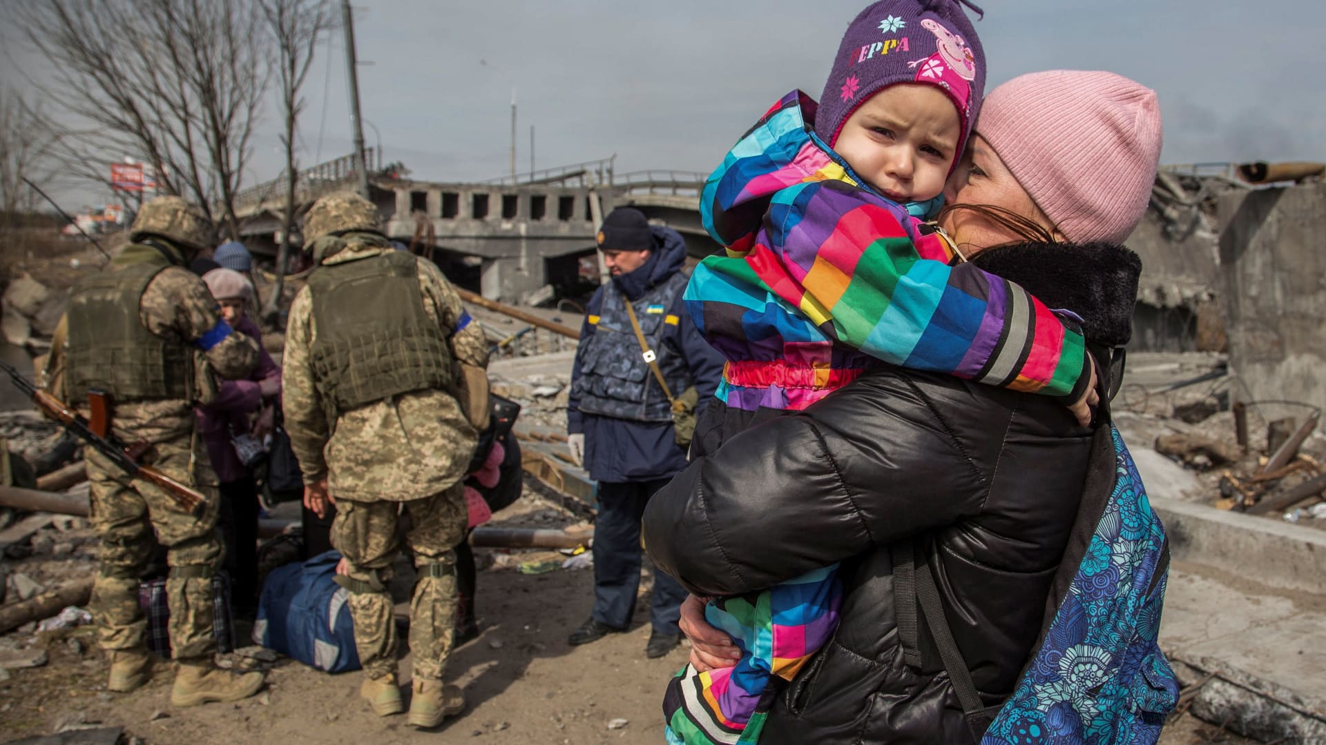 A woman holds a child next to a destroyed bridge during an evacuation from Irpin, outside of Kyiv, Ukraine, on March 28, 2022.