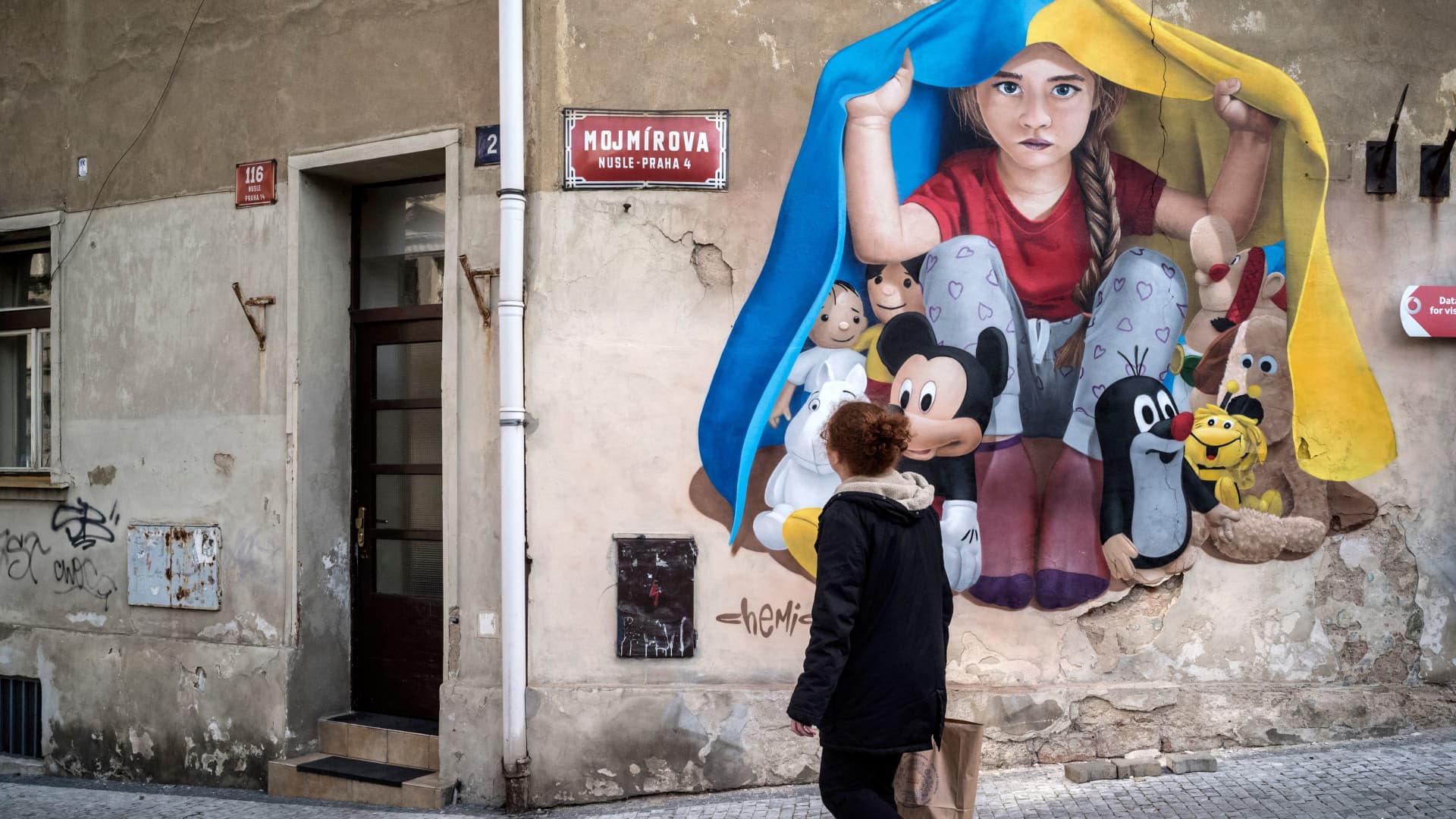 A woman walks past a graffiti mural, showing a child protecting with a Ukrainian flag against the war, made by artist ChemiS, on March 19, 2022 in Prague.