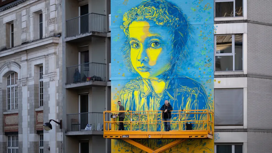 French street artist and painter Christian Guemy (R) known as C215 poses in front of his fresco depicting a Ukrainian young girl with a quote attributed to Ukrainian President Volodymir Zelensky I really don't want my photos in your offices, because I am neither a god nor an icon, but rather a servant of the Nation.