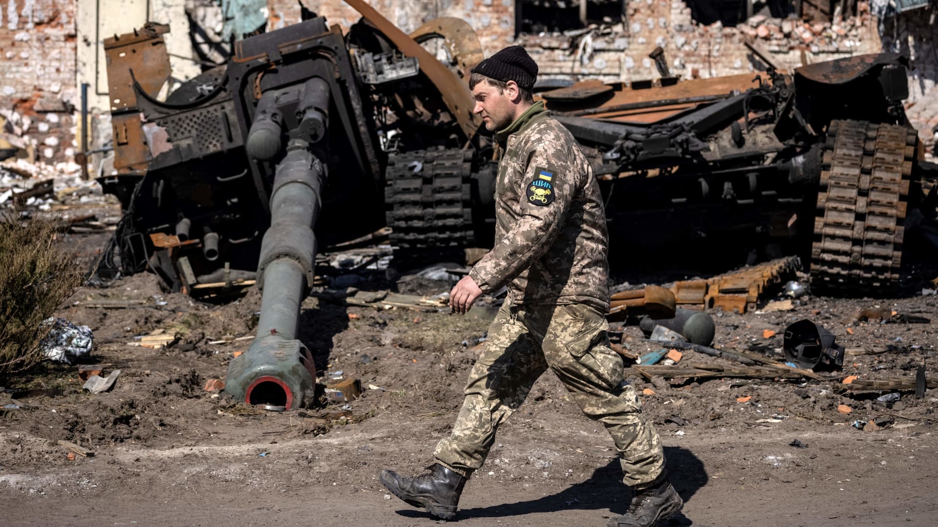 A Ukrainian serviceman walks between damaged Russian army tank and rubble of a destroyed building in the northeastern city of Trostianets, on March 29, 2022.