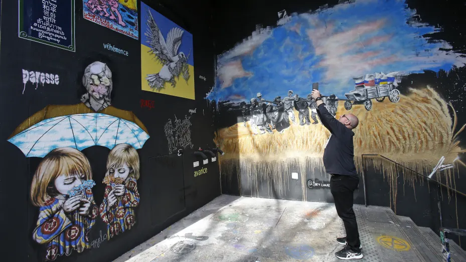 A man takes a picture of a fresco murals displayed on "The walls of peace" on March 28, 2022 in Paris France.