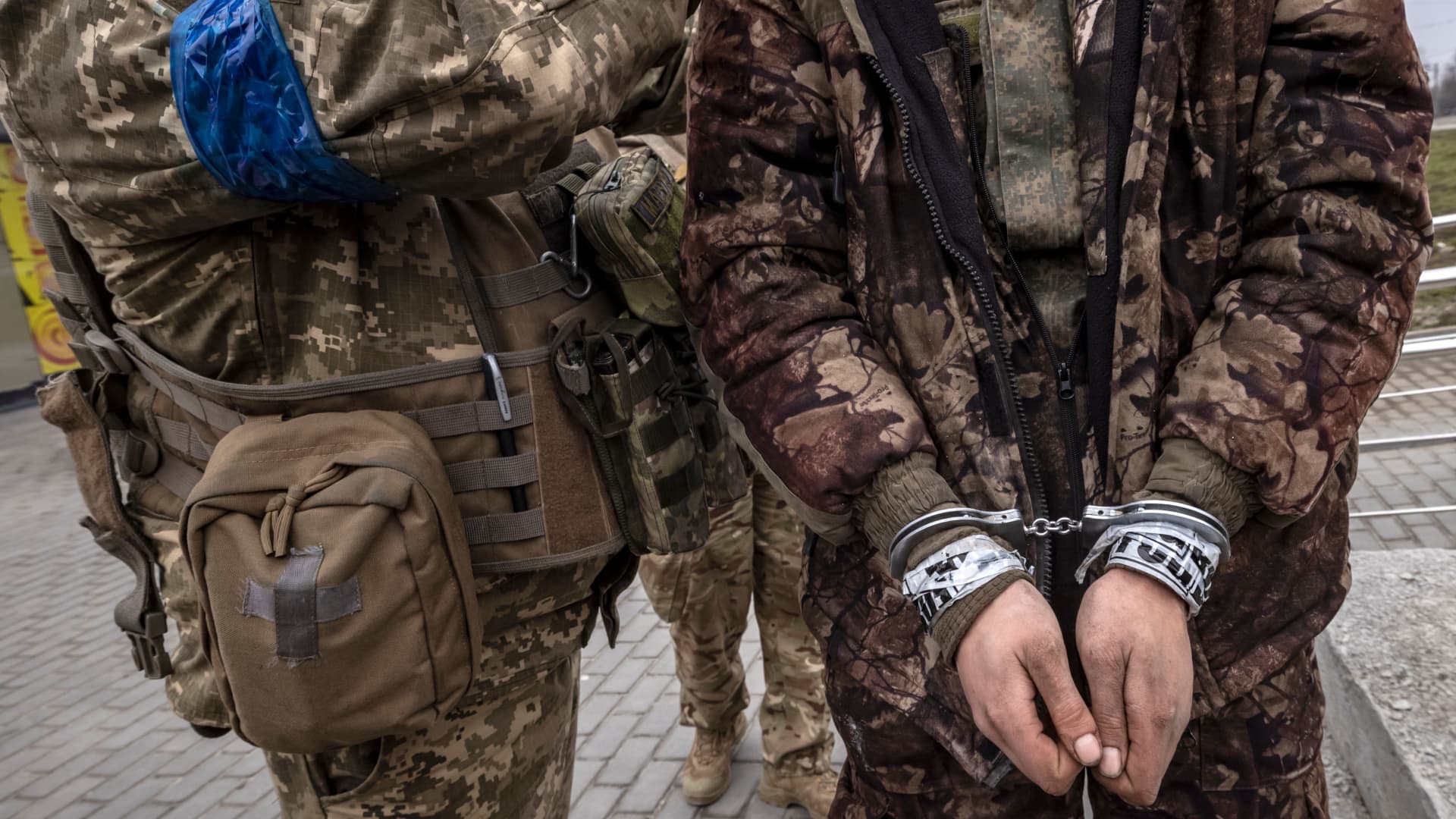 A Ukrainian serviceman stands past a handcuffed Russian soldier in Kharkiv on March 31, 2022.