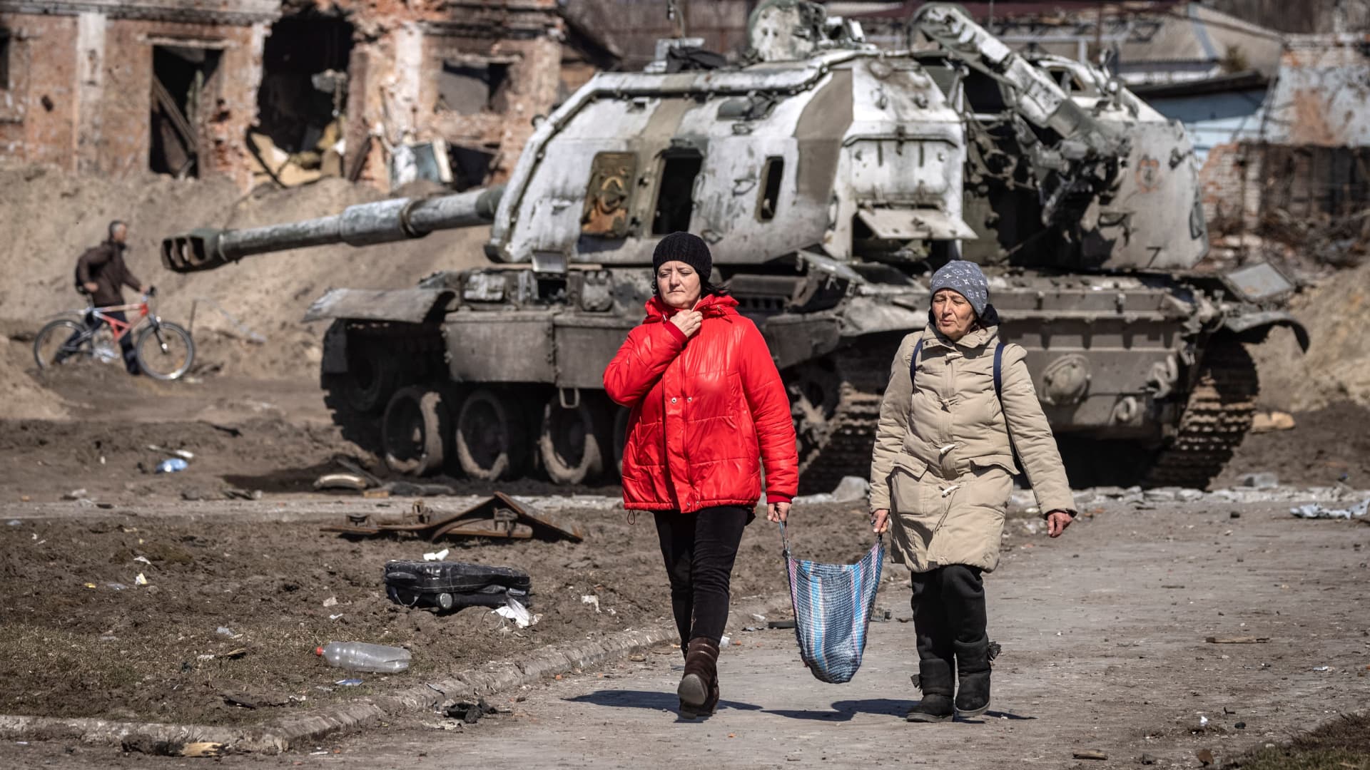 Residents walk past a damaged Russian military vehicle in the northeastern city of Trostianets, on March 29, 2022.