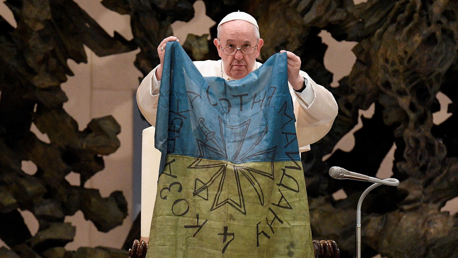 Pope Francis holds the Ukrainian flag that was sent to him from the town of Bucha, where tied bodies of civilians who were shot at close range, a mass grave and other signs of executions were found, during the weekly general audience at the Paul VI Hall at the Vatican, April 6, 2022. 