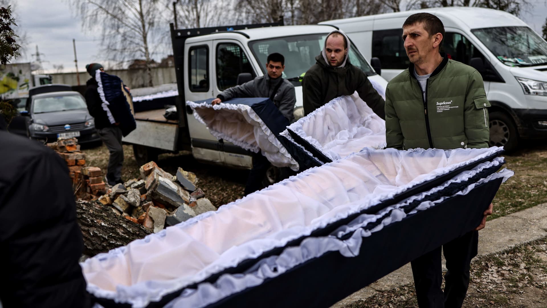Workers bring coffins where bodies are transported for identification by forensic personnel and police officers in the cemetery in Bucha, north of Kyiv, on April 6, 2022, after hundreds of civilians were found dead in areas from which Russian troops have withdrawn around Ukraine's capital, including the town of Bucha.
