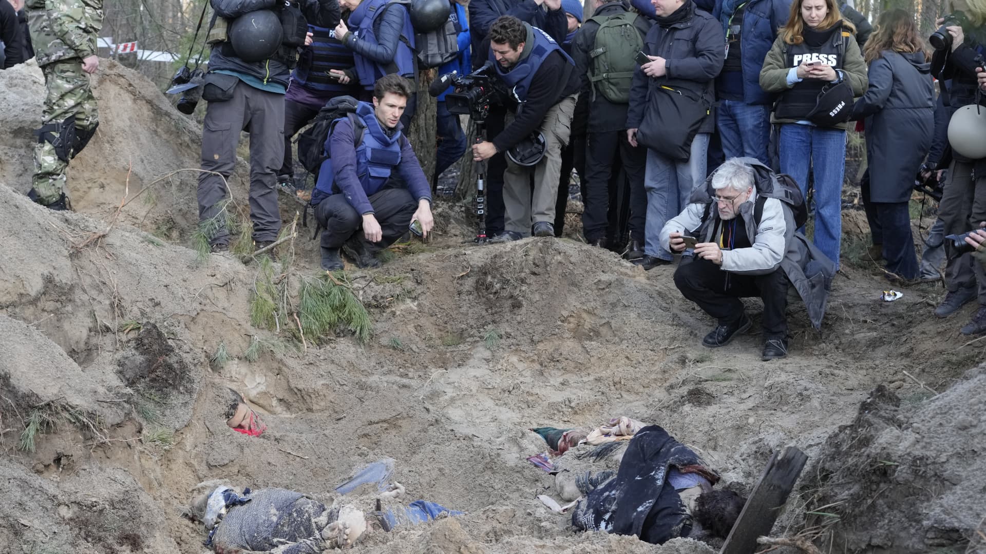 Journalists stand on the side of a mass grave of village residents and the village head and his family, in the village of Motyzhyn, close to Kyiv, Ukraine, Monday April 4, 2022.