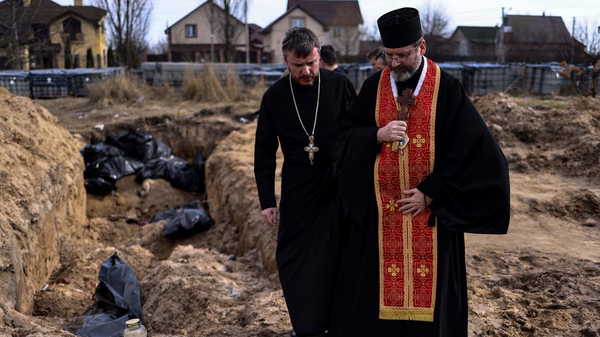 Priests pray at body bags in a mass grave in the garden surrounding the St Andrew church in Bucha, on April 7, 2022, amid Russia's military invasion launched on Ukraine.