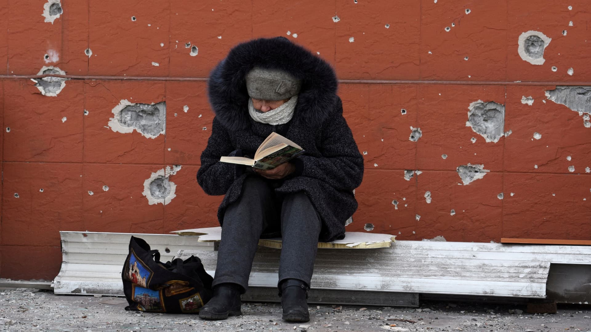 A local resident reads a book near a building damaged in the course of Ukraine-Russia conflict in the southern port city of Mariupol, Ukraine April 3, 2022.