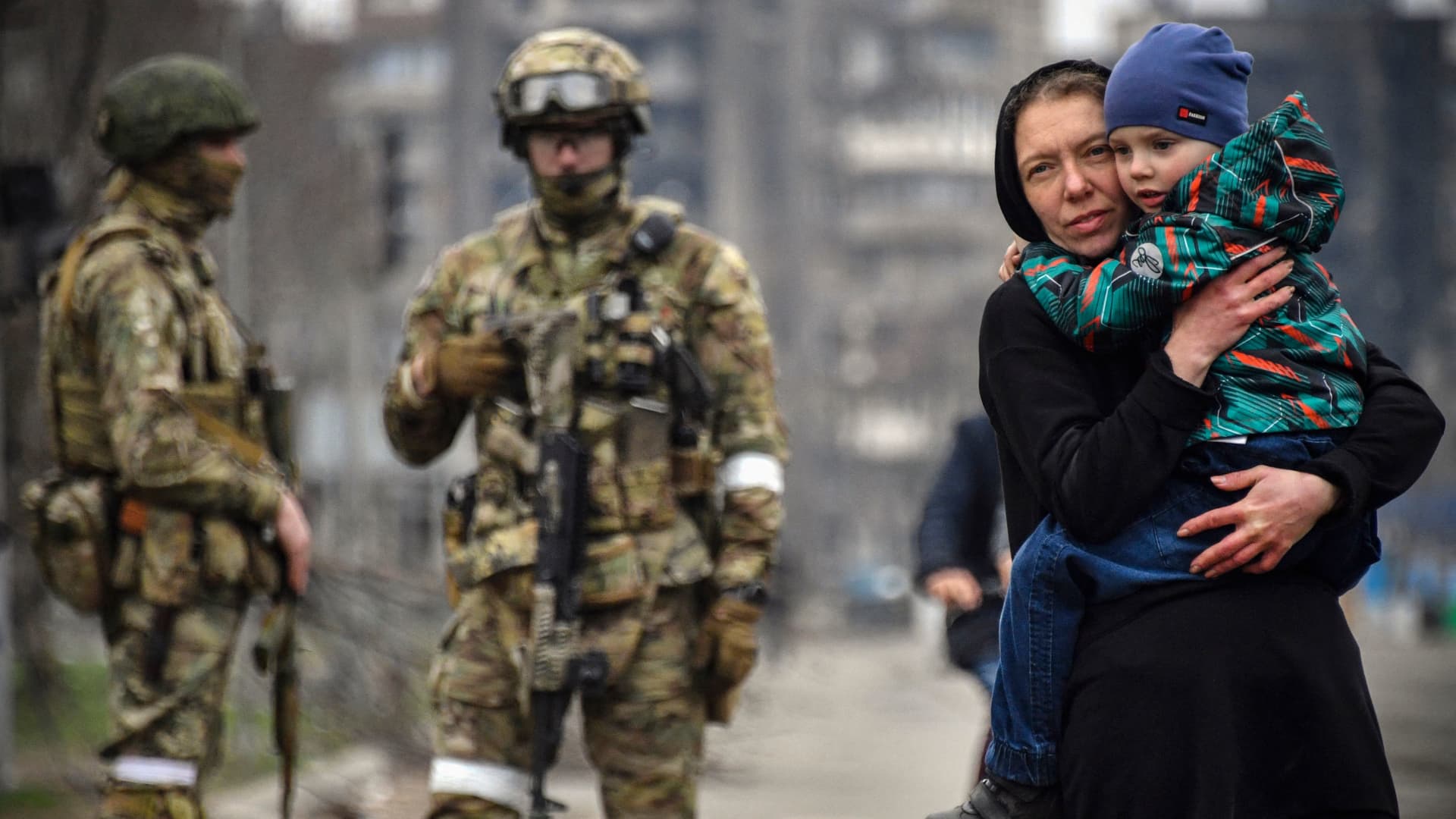 A woman holds a child next to Russian soldiers in a street of Mariupol on April 12, 2022, as Russian troops intensify a campaign to take the strategic port city, part of an anticipated massive onslaught across eastern Ukraine, while Russia's President makes a defiant case for the war on Russia's neighbour. - *EDITOR'S NOTE: This picture was taken during a trip organized by the Russian military.*