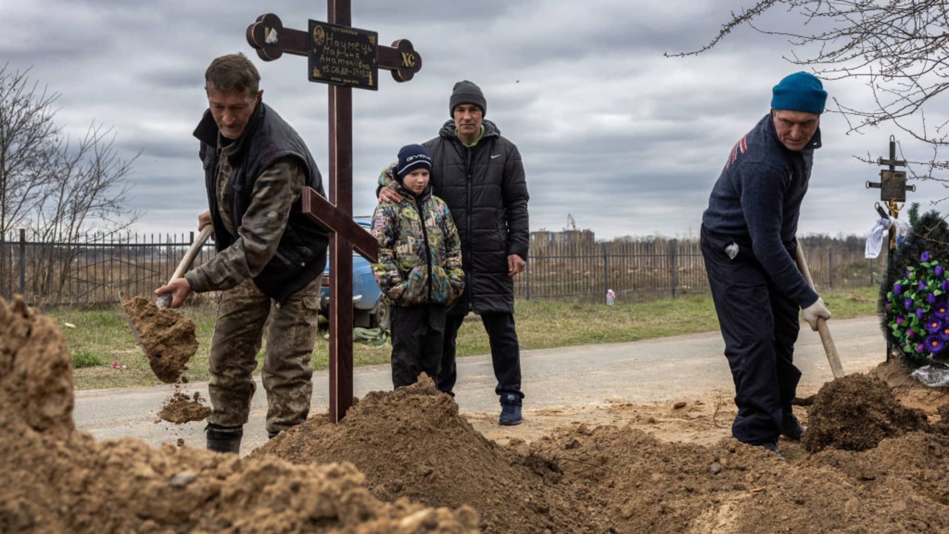 Grave diggers shovel soil into the grave of a woman as her husband and son watch on April 20, 2022 in Bucha, Ukraine.