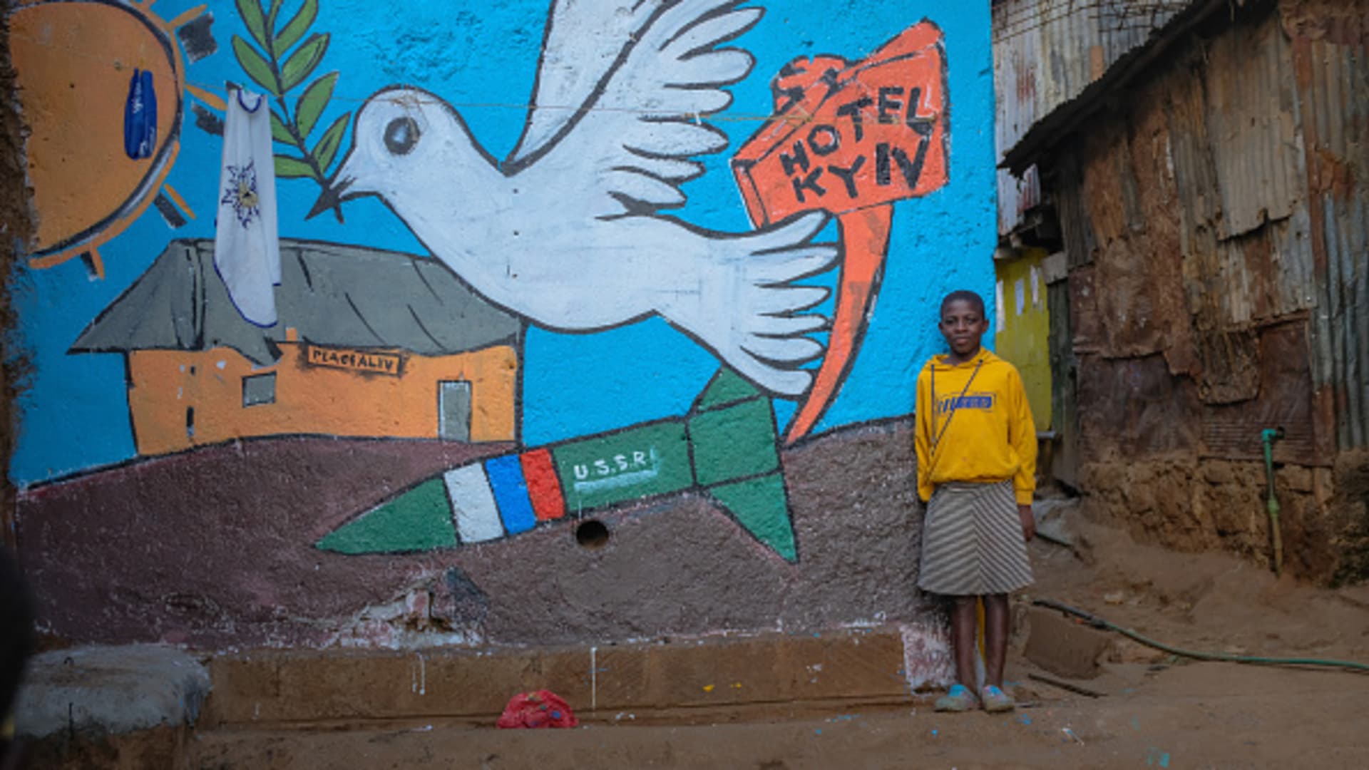 A girl poses by a street mural created by a group of Artists from Maasai Mbili depicting a sign of love from Kibera to Ukraine a midst the war.