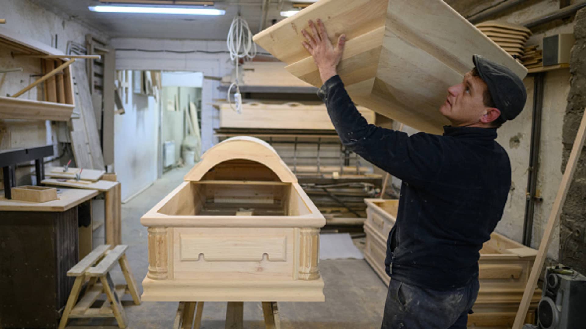 Craftsman Ruslan Slyusar attaches hingers to the lid of a coffin at a coffin workshop on April 28, 2022 in Rava-Ruska, Ukraine.