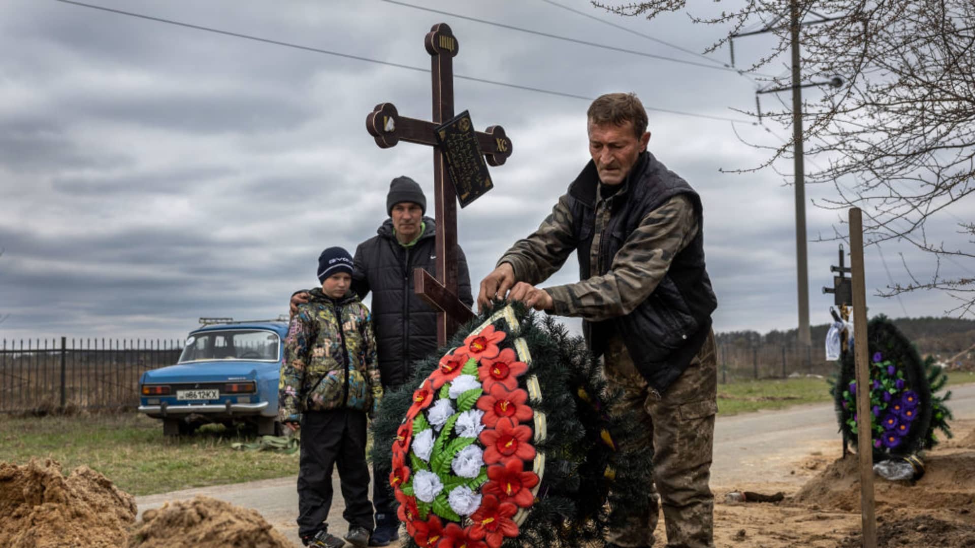 A grave digger arranges flowers atop the grave of a woman as her husband and son watch on April 20, 2022 in Bucha, Ukraine. Ukraine's prosecutor general Iryna Venediktova has identified 10 Russian soldiers she previously accused of atrocities in Bucha, Ukraine, The Associated Press reported.