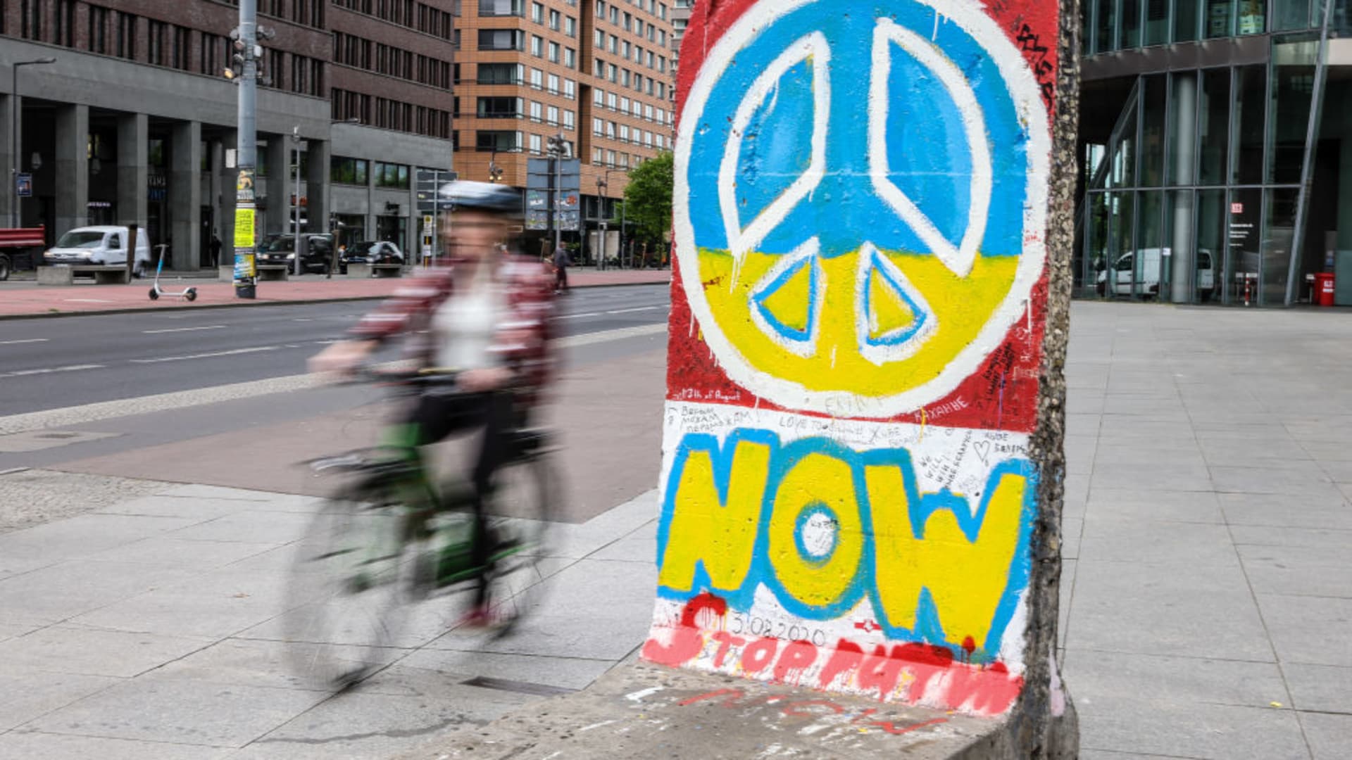 A cyclist passes by a part of the Berlin Wall decorated with a graffiti of a Ukrainian flag colored Peace symbol, expressing solidarity with Ukraine at Potsdamer Platz on May 4, 2022 in Berlin, Germany.