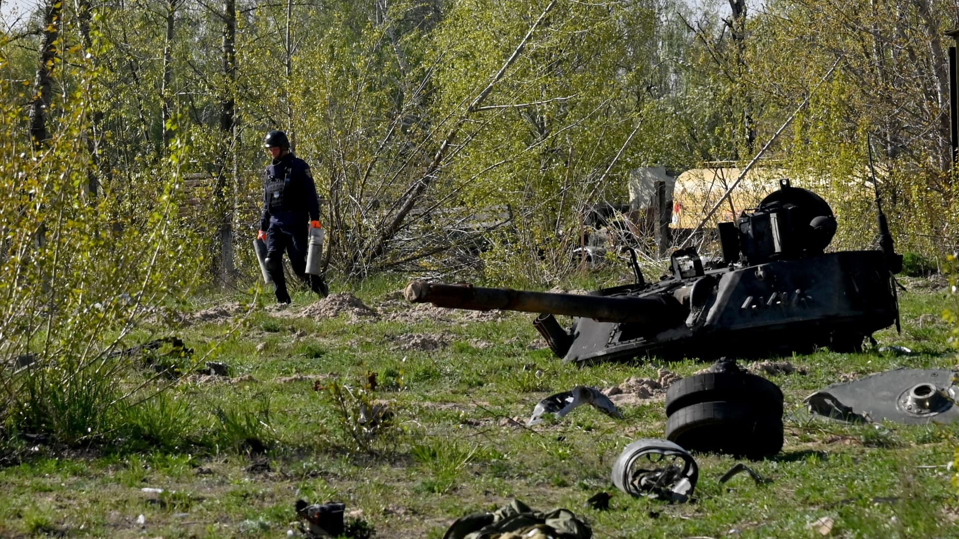 A Ukrainian deminer carries unexploded material as he walks past a destroyed tank during demining works at an airport in the town of Hostomel, northwestern of Kyiv, on May 5, 2022. 