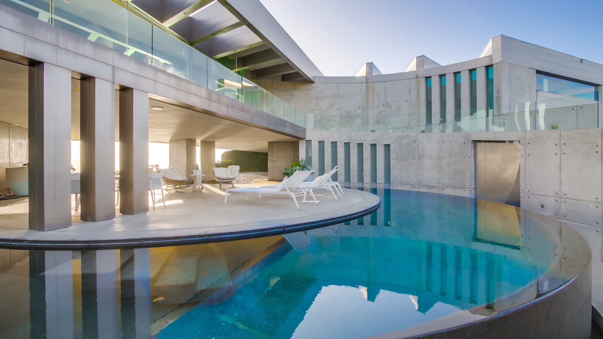 A crescent-moon shaped infinity pool wraps around a circular terrace.