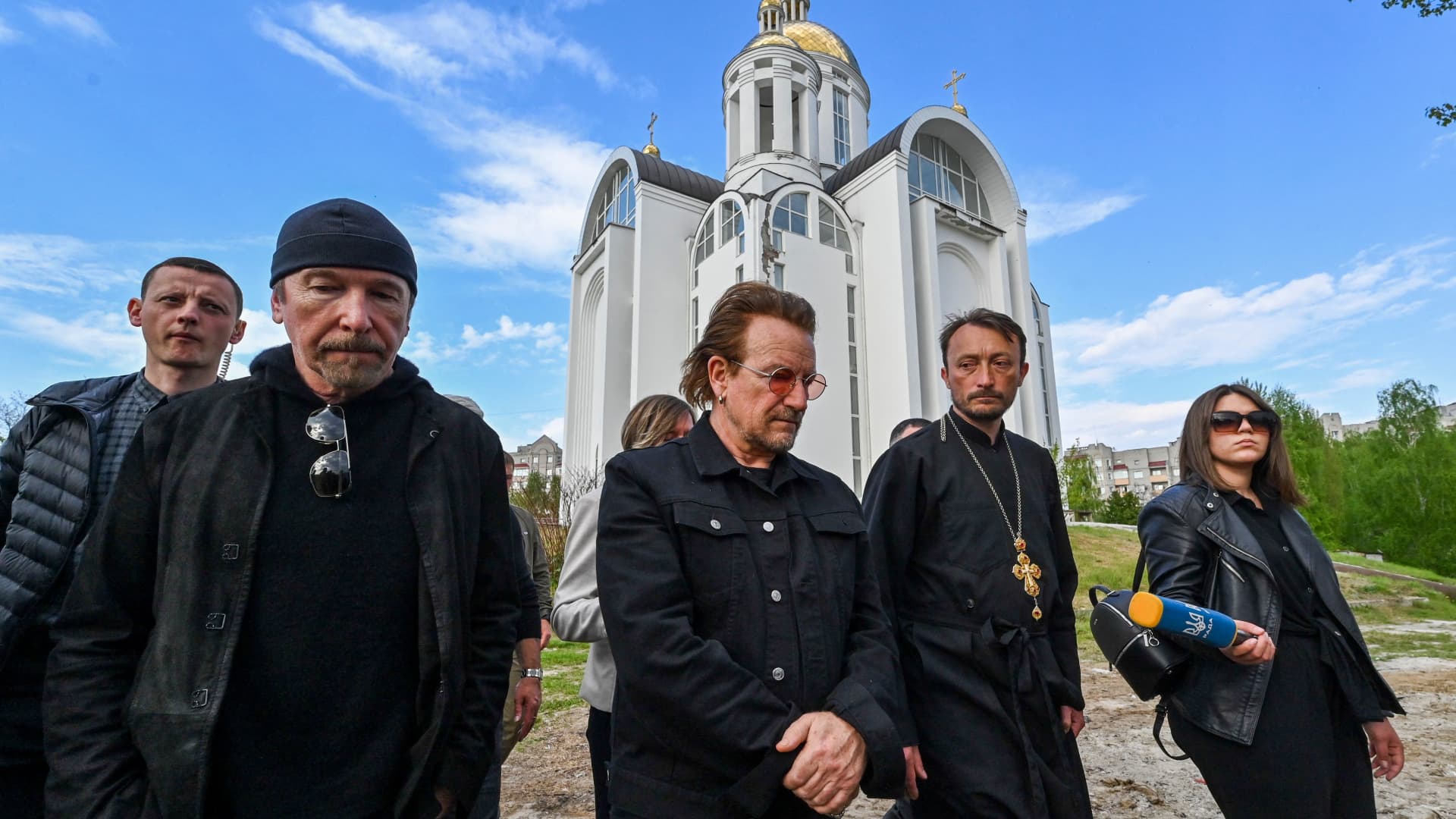 Andrii Holovine, priest of the Church of St. Andrew Pervozvannoho All Saints (2nd,R) guides Bono (C) (Paul David Hewson), activist and front man of the Irish rock band U2 and guitarist David Howell Evans aka 'The Edge' (R) visiting the site of a mass grave by the church in the Ukrainian town of Bucha, near Kyiv on May 8, 2022.