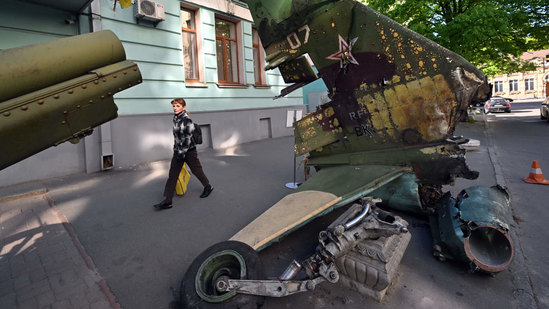 A pedestrian passes in front of the wreckage of a Russian plane outside the National Museum of Military History of Ukraine in Kyiv on May 5, 2022. - The exhibit's curator Pavlo Netesov hopes the freshly destroyed equipment will serve as a visible reminder of the war's toll to residents in downtown Kyiv -- who have been largely spared from the harsh ground fighting that has erupted elsewhere across the country.