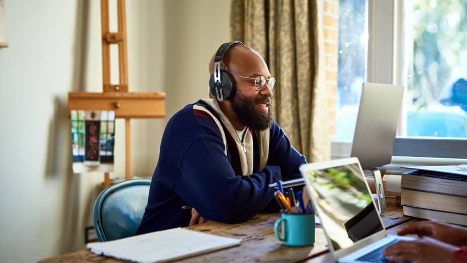 Black businessman wearing headphones in front of laptop, talking handsfree, working from home, busy, teleworking