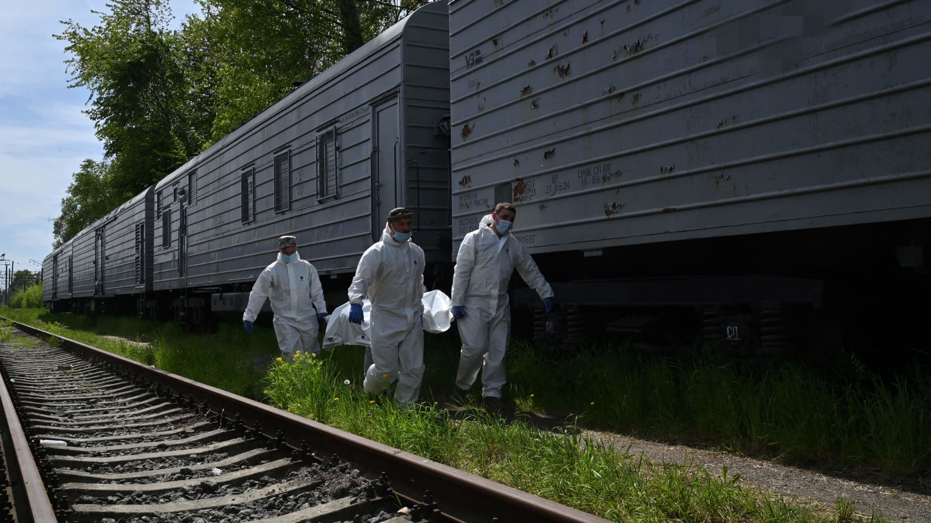Ukrainian forensics experts carry the body of a Russian soldier exhumed in the village of Zavalivka, west of Kyiv, before it is stored in a refrigerated rail car stacked with the Russian dead on May 11, 2022.