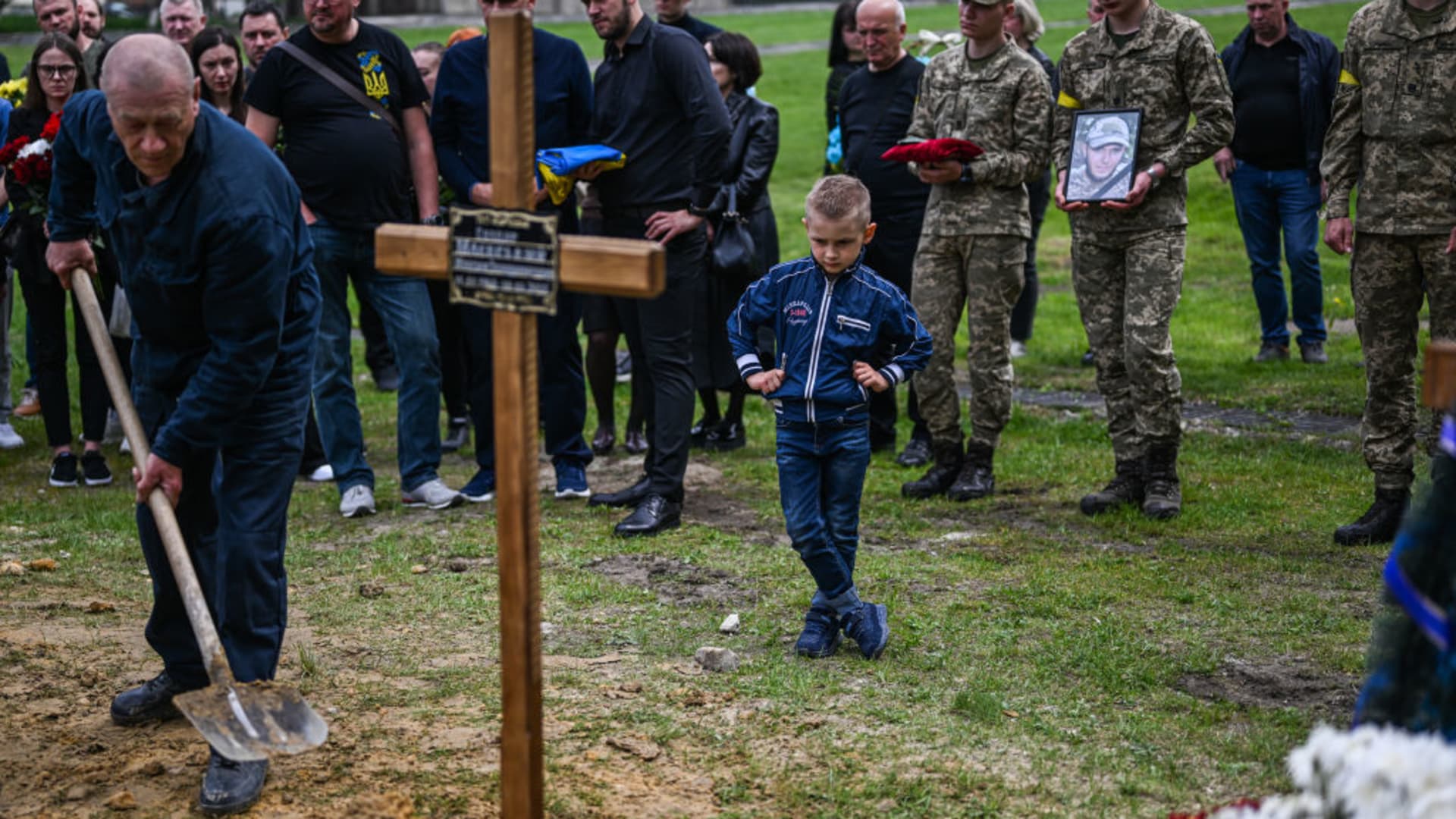 A child watches grave diggers putting soil on the grave of the the fallen sniper, Maxim Mayevsky, age 34 mourn during his funeral at the Field of Mars of Lychakiv cemetery in Lviv, Ukraine on May 13, 2022.
