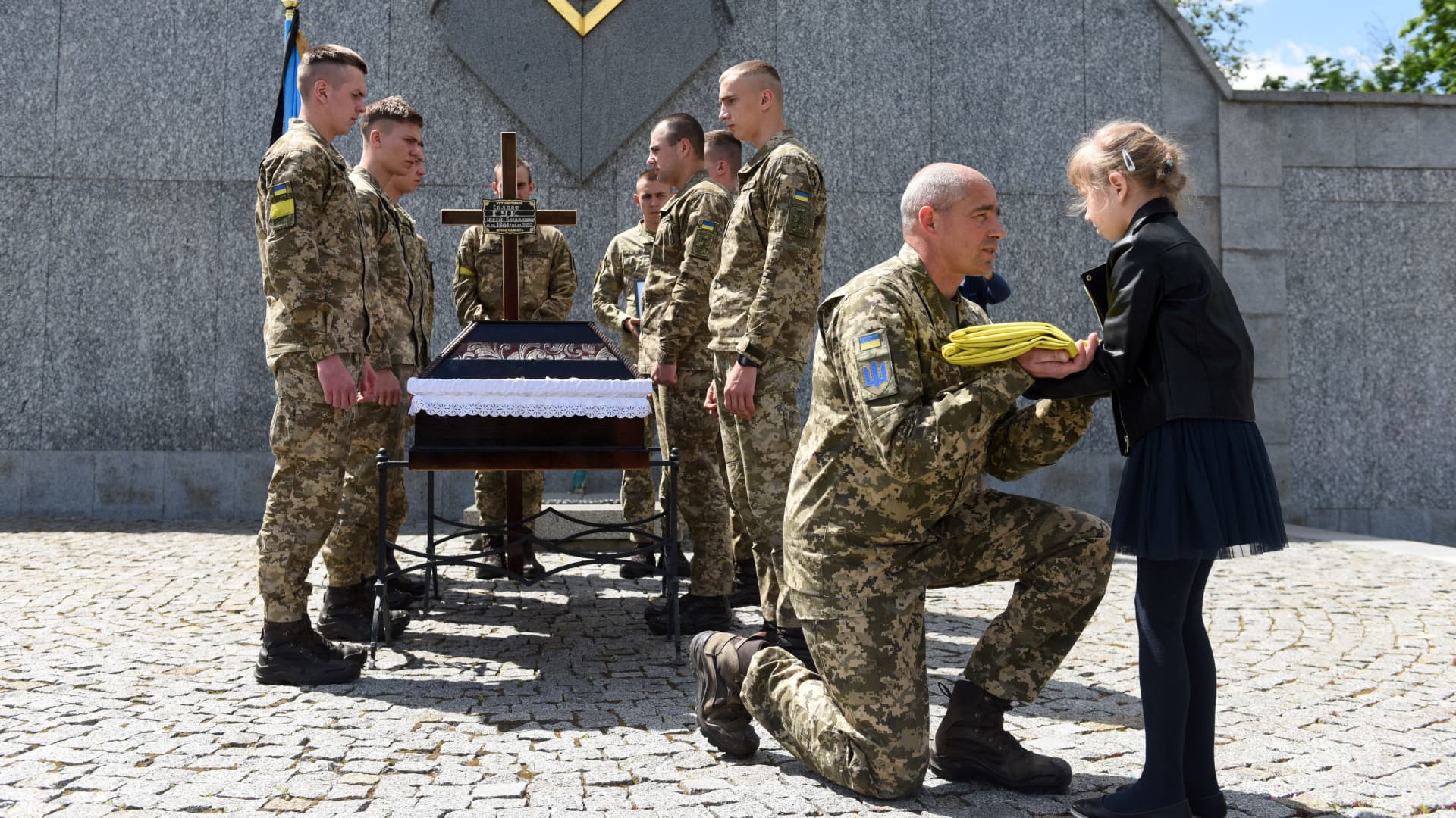A serviceman offers the Ukrainian flag to the daughter of Yuriy Huk, a Ukrainian serviceman, killed during the Russian invasion of Ukraine, at his funeral service at the Saints Peter and Paul Garrison Church, in the western Ukrainian city of Lviv on May 16, 2022.