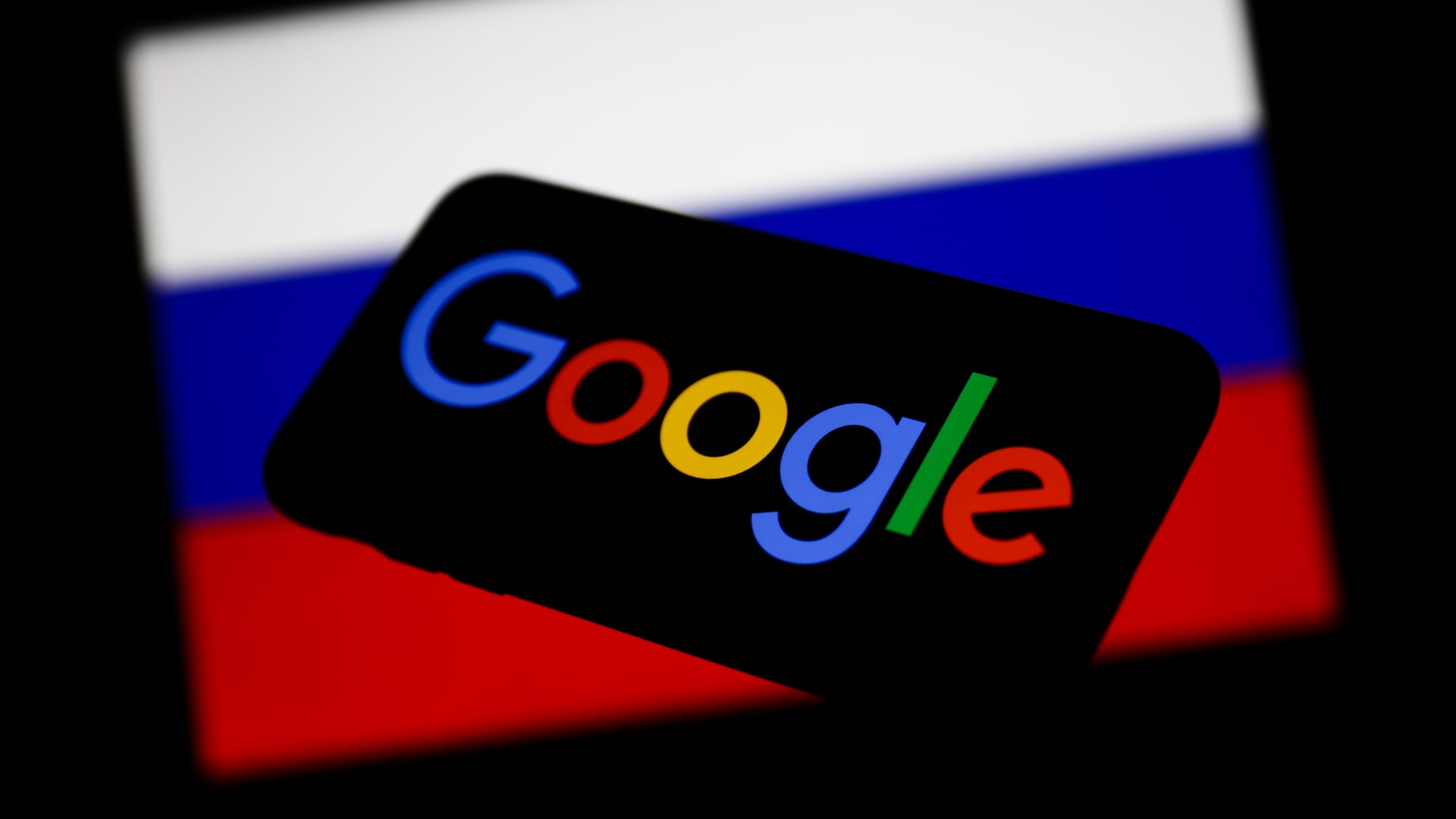 Google logo displayed on a phone screen and Russian flag displayed on a screen in the background are seen in this illustration photo on March 1, 2022. Google's Russian subsidiary is planning to file for bankruptcy after authorities seized its bank account, said a Google spokesperson cited by Reuters, but free services like search and YouTube will remain available for Russian users.