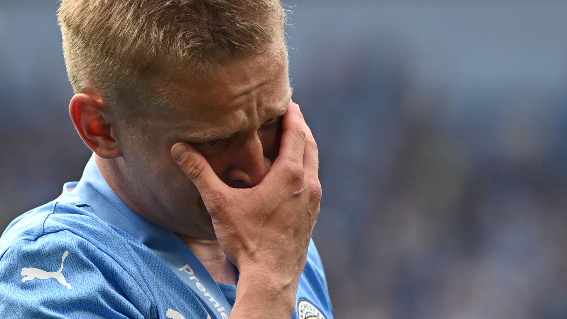 Manchester City's Ukrainian midfielder Oleksandr Zinchenko reacts to seeing the Ukrainian flag on the trophy as City players celebrate on the pitch after the English Premier League football match between Manchester City and Aston Villa at the Etihad Stadium in Manchester, north west England, on May 22, 2022. 